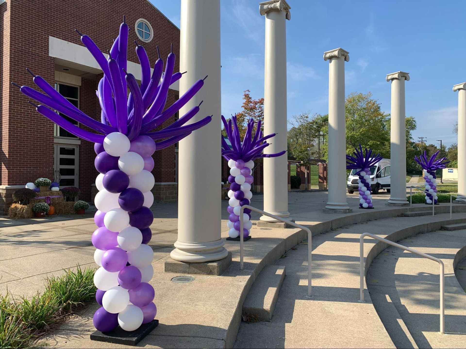 Purple and white balloons are arranged in the shape of palm trees