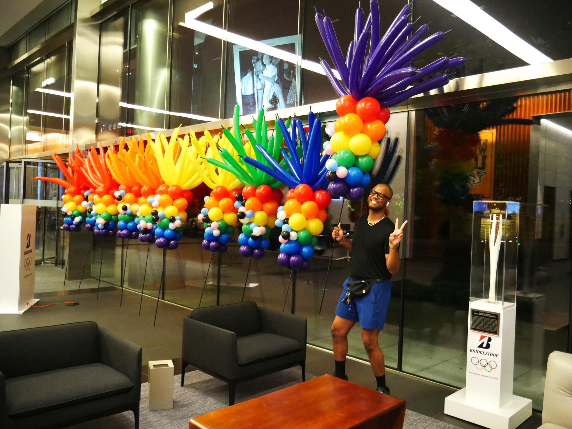 A man is standing in front of a rainbow colored balloon display.
