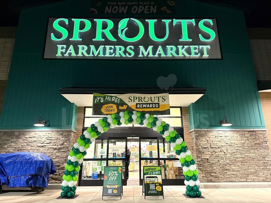 Sprouts Farmers Market store front at night with a green and white balloon arch over the entrance.