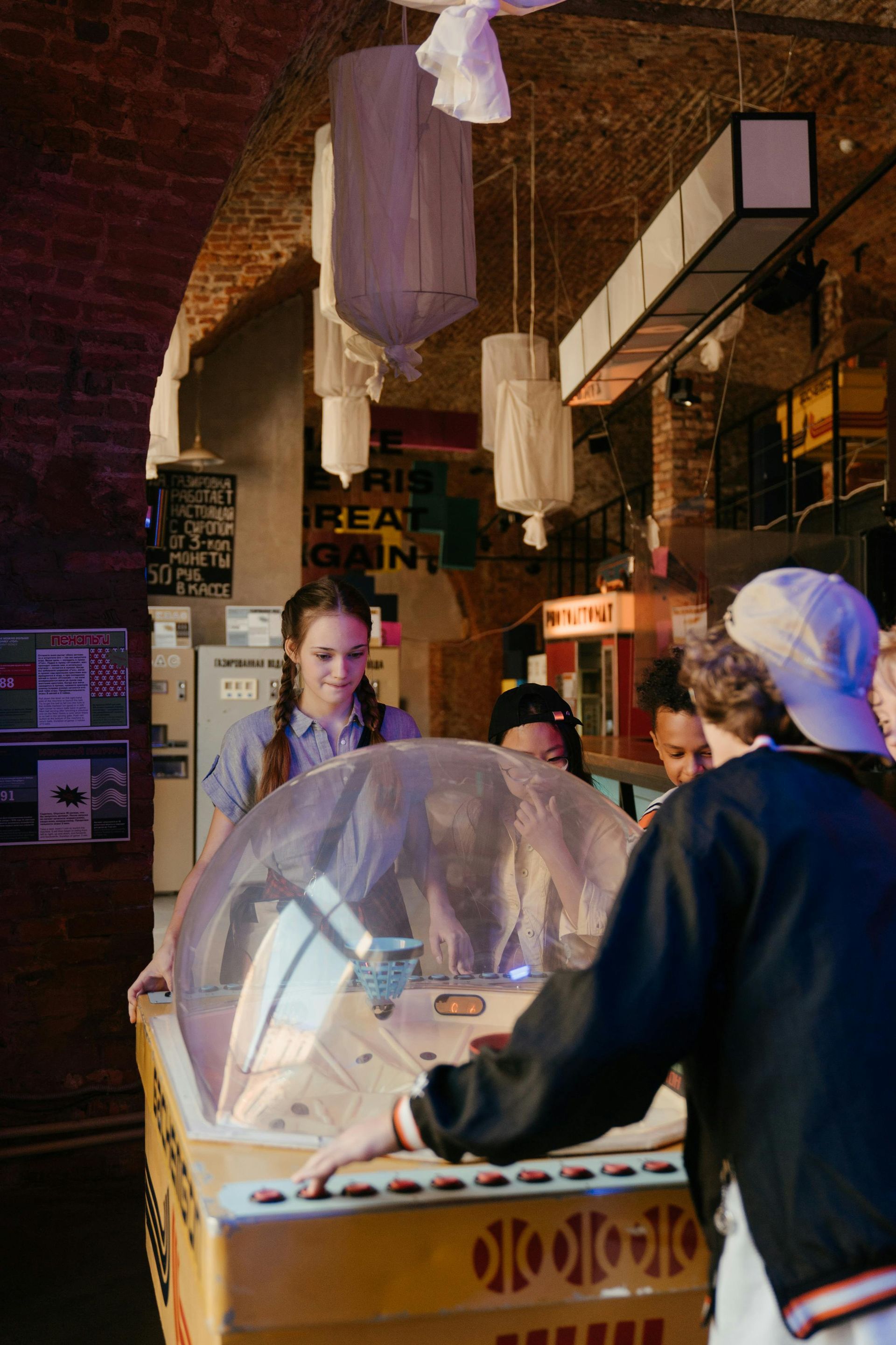 A group of people are playing a pinball machine in a room.