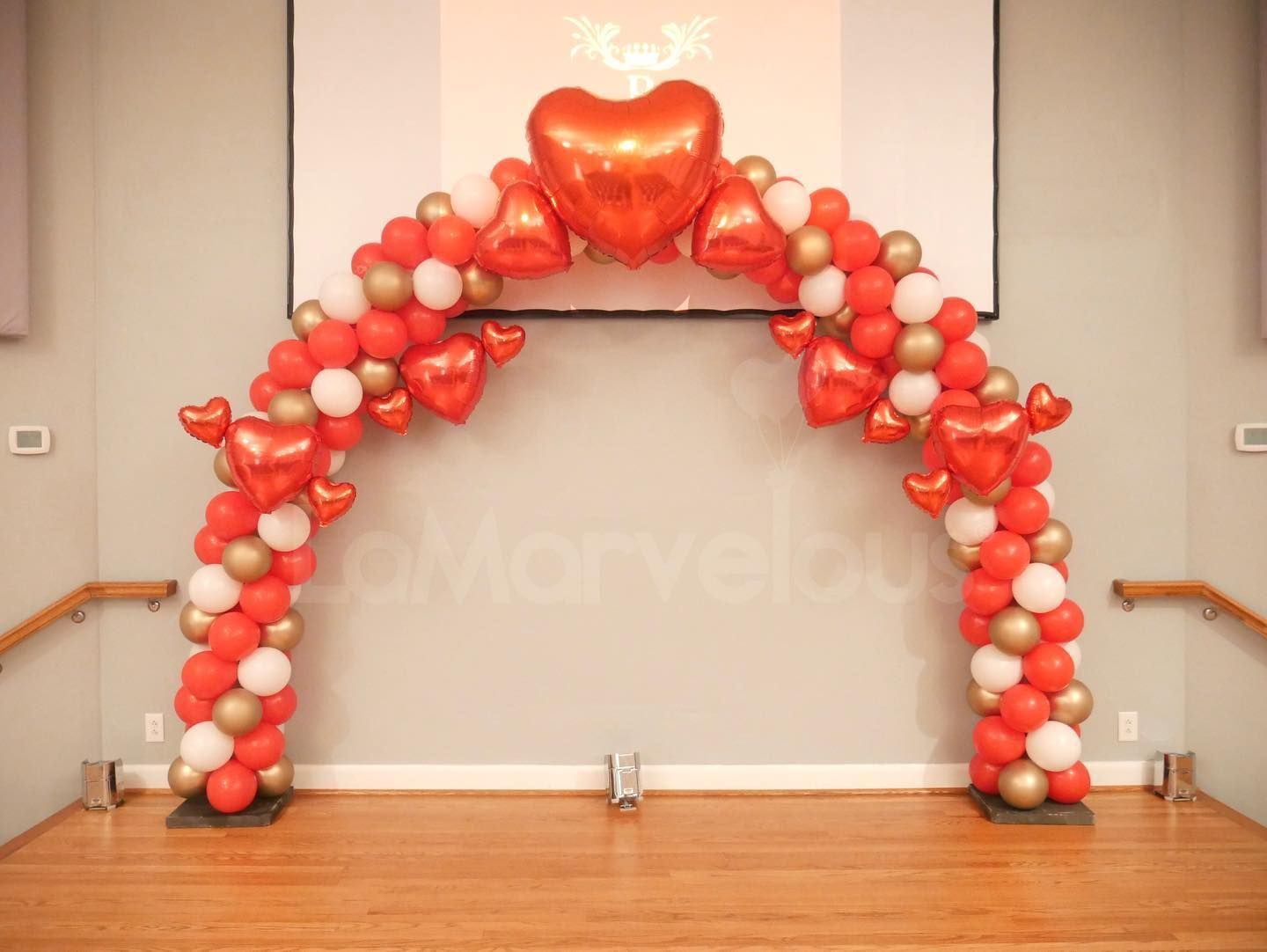 A red and gold balloon arch with a heart shaped balloon in the middle