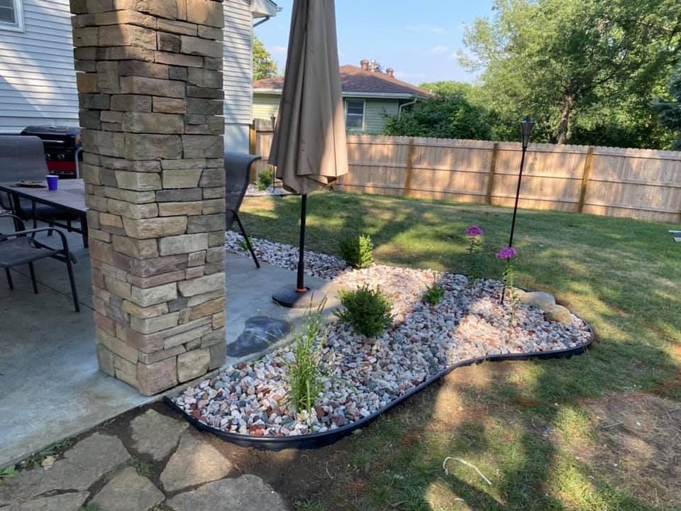A backyard with a stone pillar , umbrella , table and chairs.