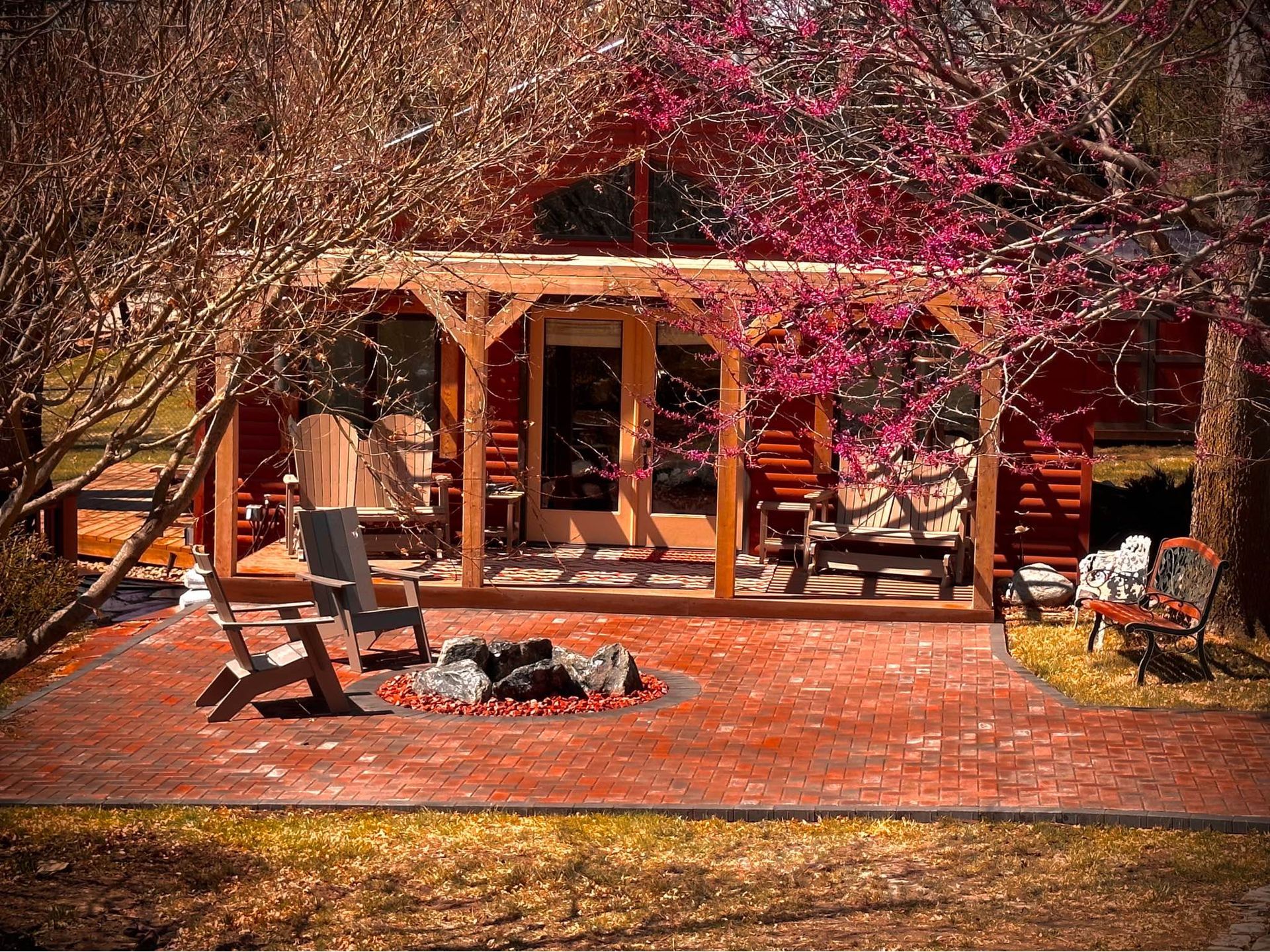 A cabin with a fire pit in front of it surrounded by trees and flowers.