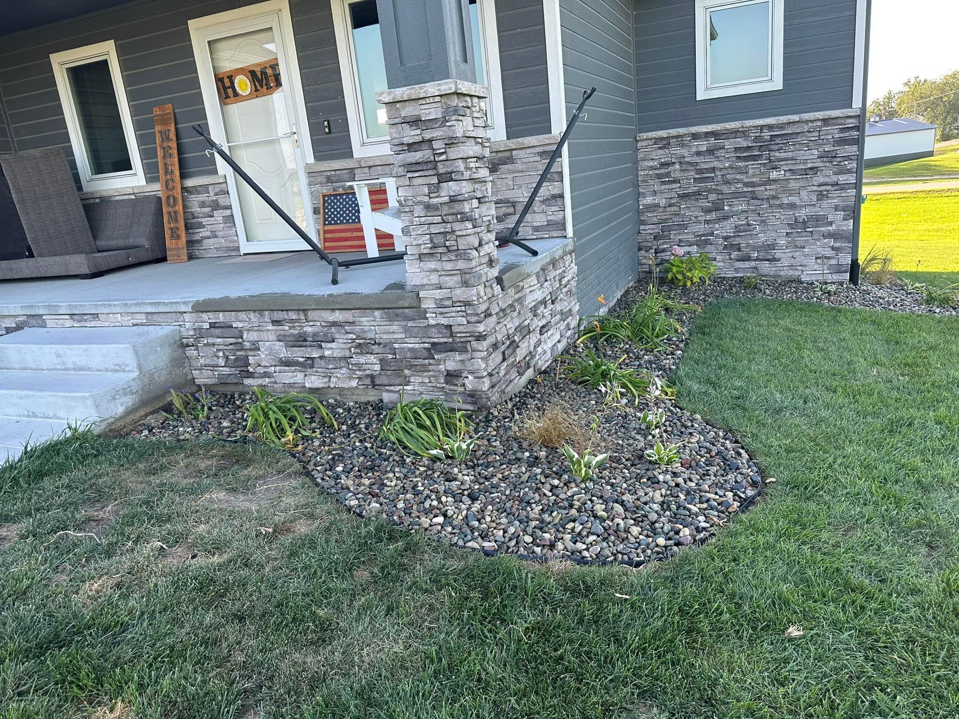 A house with a stone porch and stairs is sitting on top of a lush green lawn.