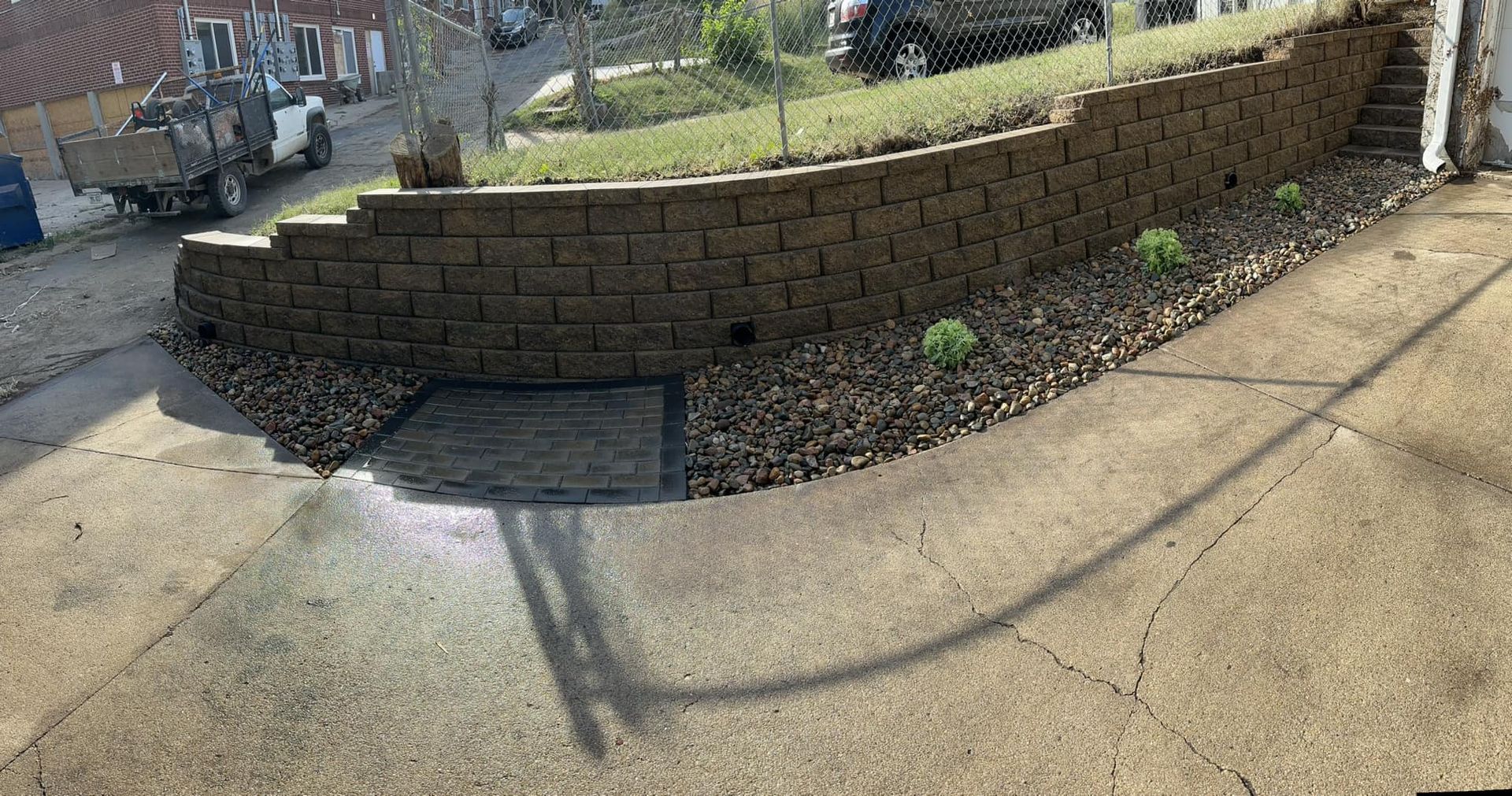 A brick wall is sitting on top of a concrete driveway next to a sidewalk.