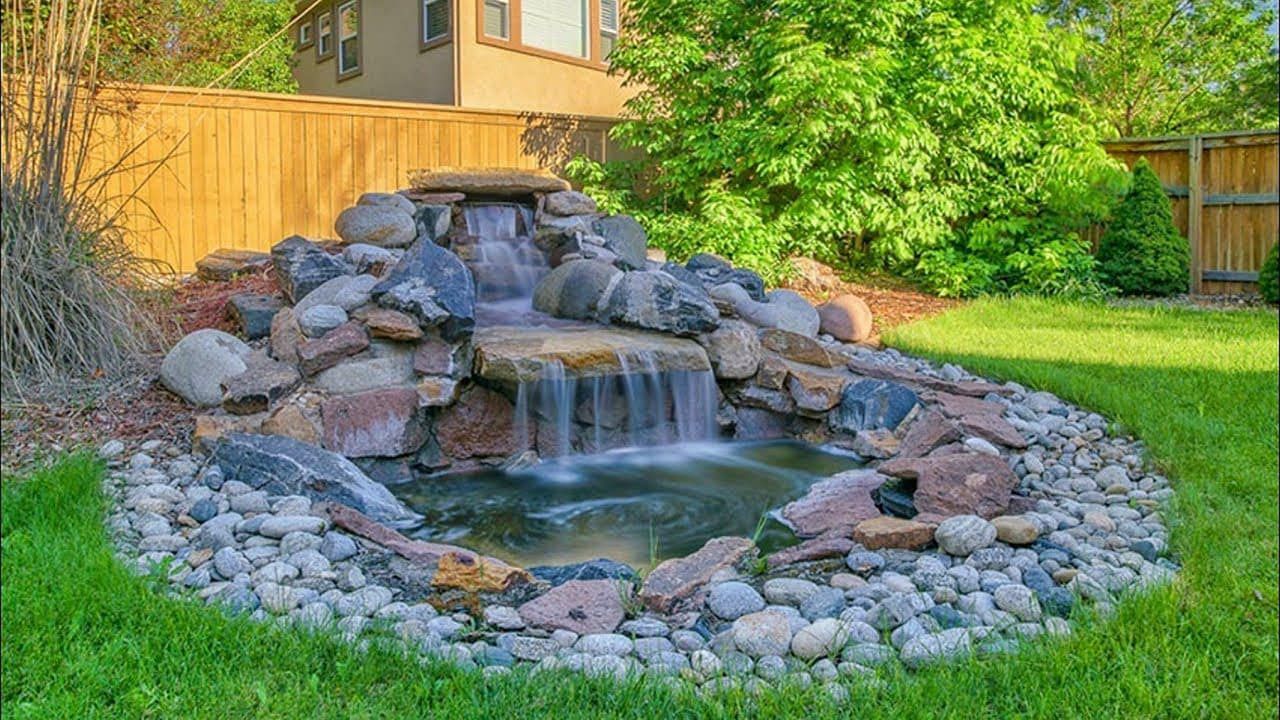 A waterfall is surrounded by rocks and a pond in a backyard.