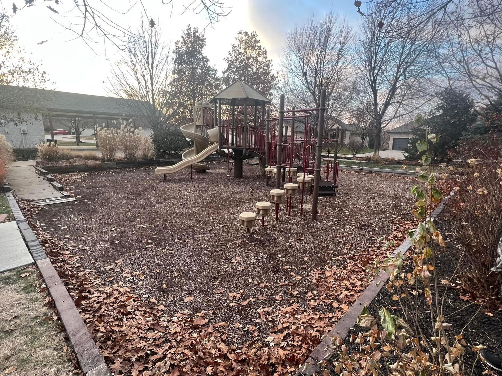 There is a playground in the middle of a park covered in leaves.