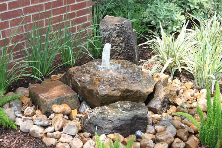 A small fountain is surrounded by rocks and plants in a garden.