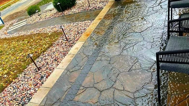 A patio with chairs and a bench in the rain.