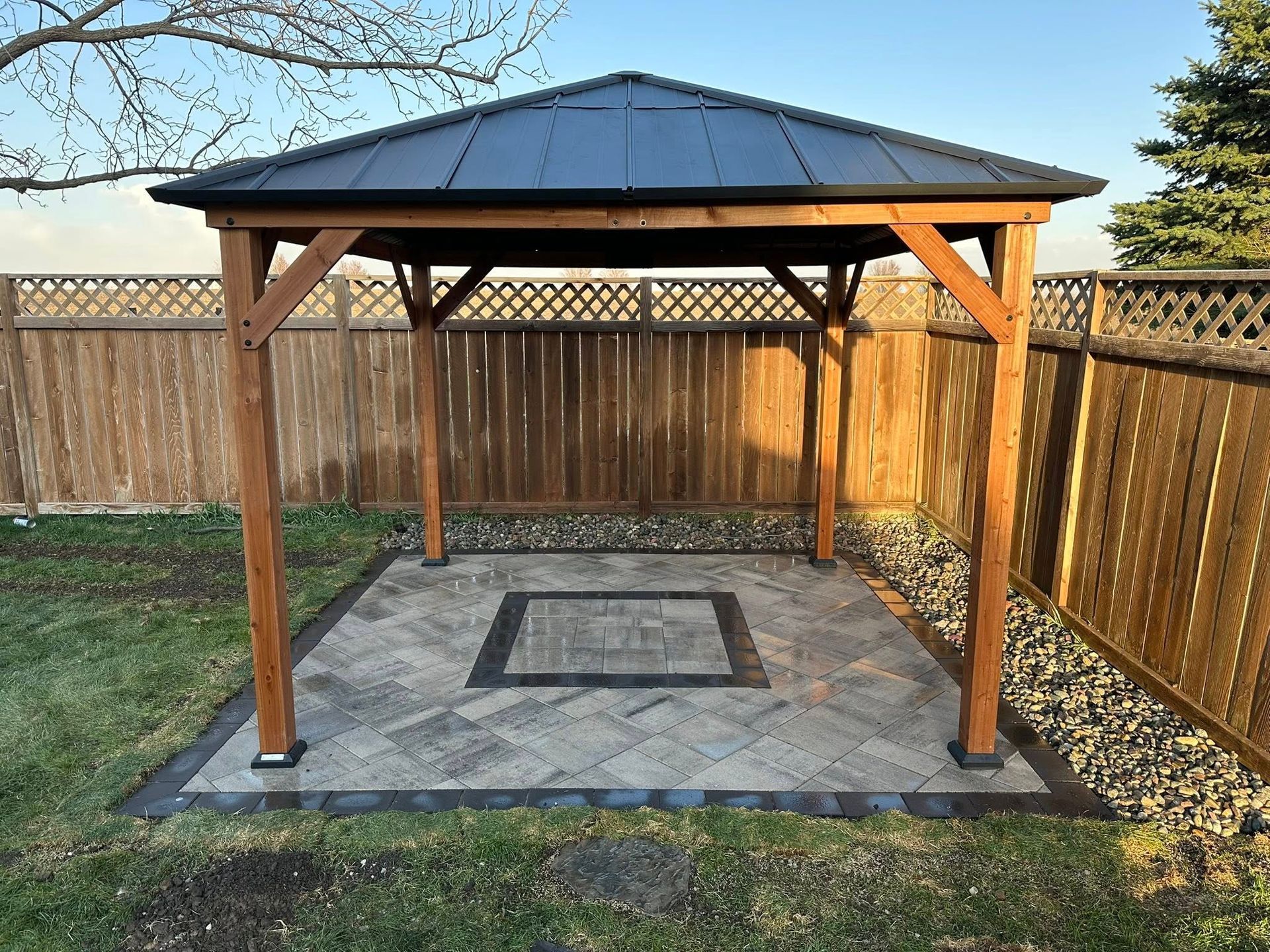 A gazebo is sitting in the middle of a backyard next to a wooden fence.