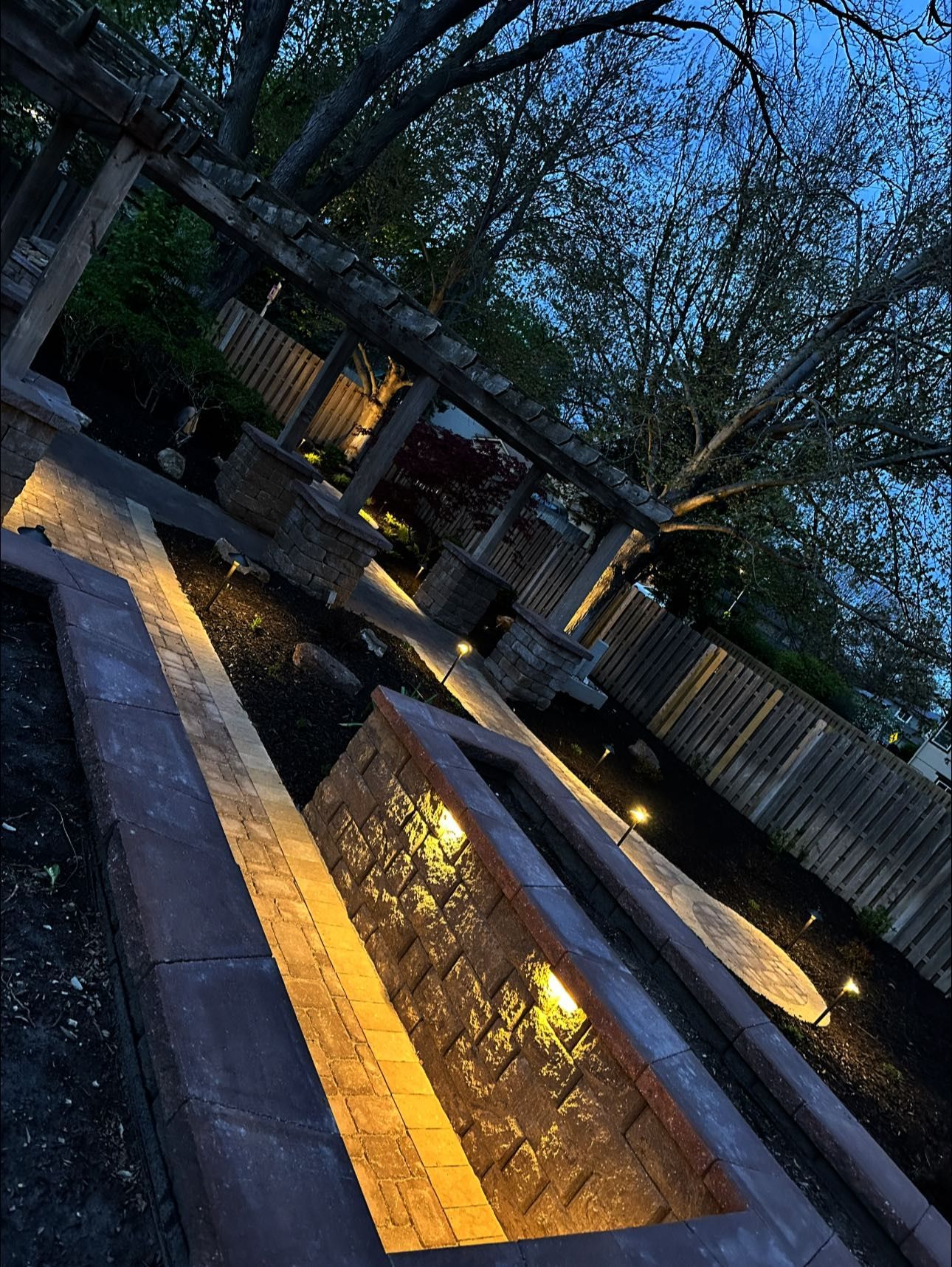 A fenced in area with a pond and a pergola at night