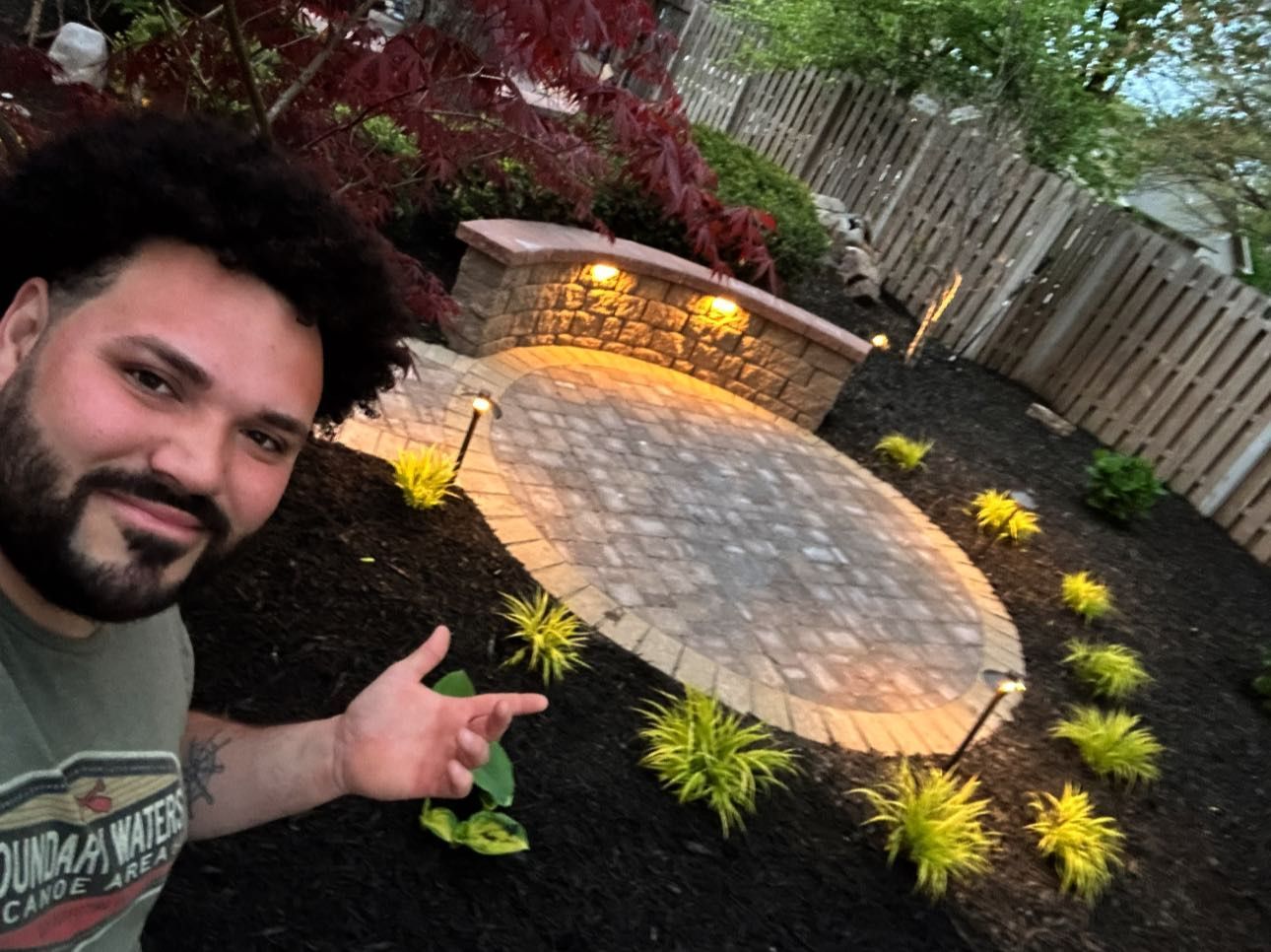 A man with a beard is standing in front of a brick patio.