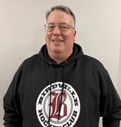 Smiling man in a black hoodie with a circular logo, standing against a plain white background
