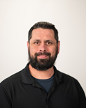 Portrait of a smiling man with a beard, wearing a black shirt against a light background