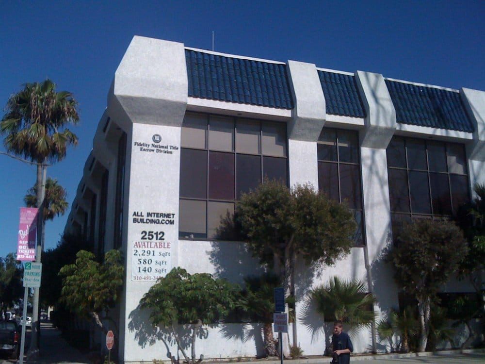 White office building with dark blue roof trim and palm trees.