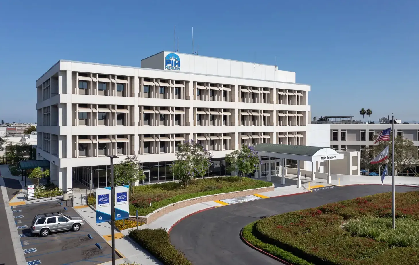 Hospital exterior with blue sky. Multi-story beige building with windows and curved driveway.