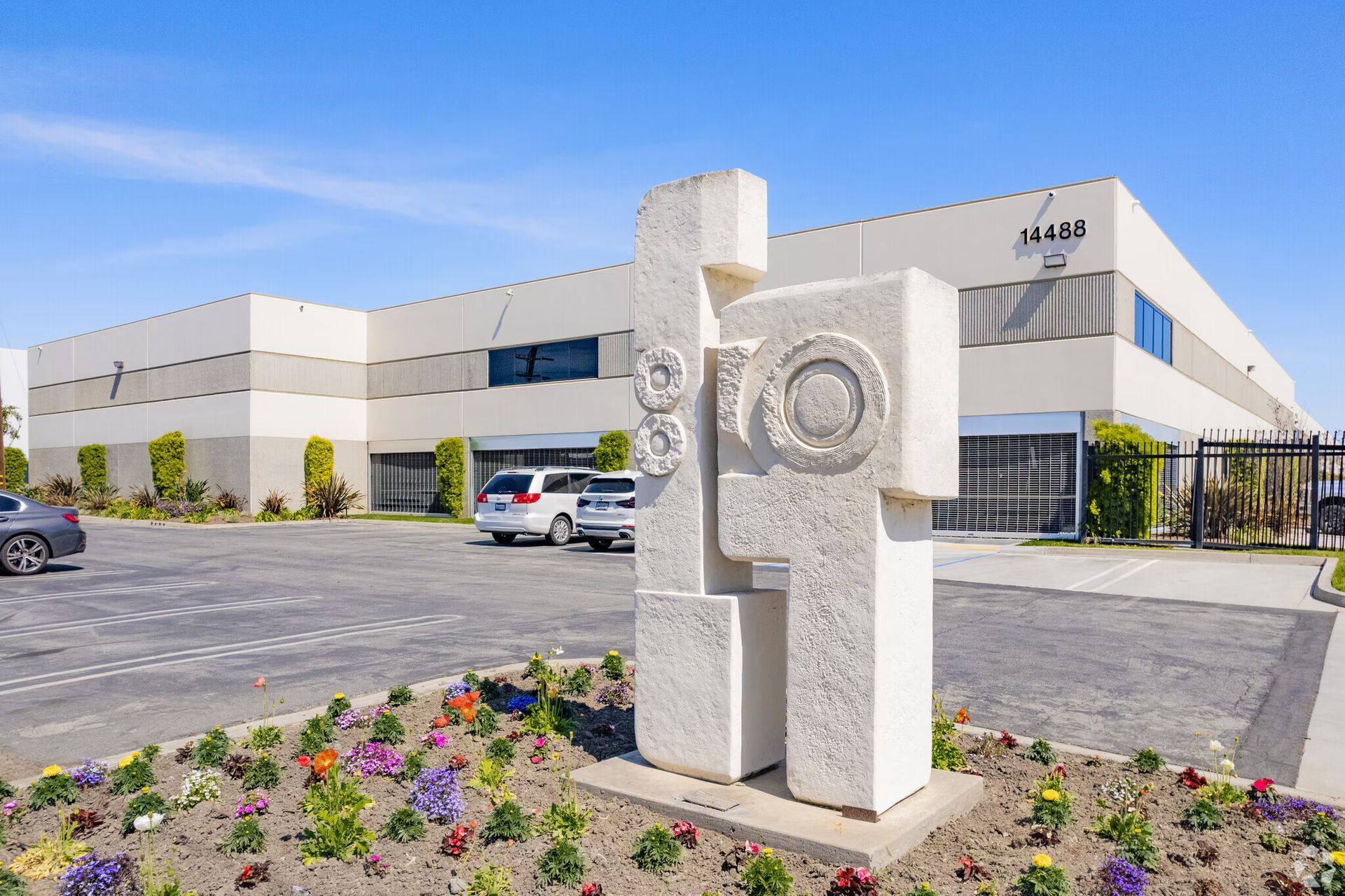 A modern beige commercial building with a sculpture in front and a flower bed.
