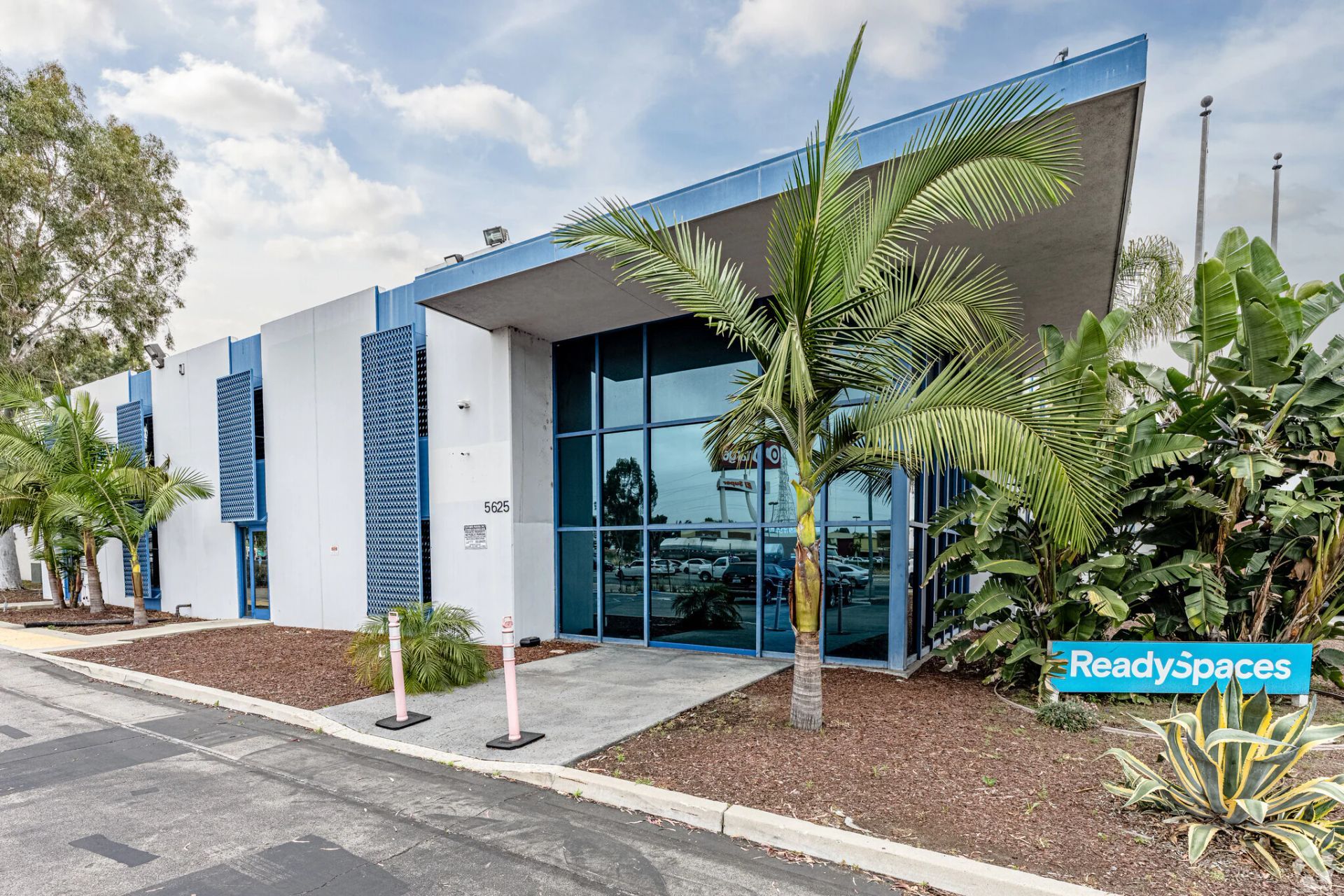 Modern office building with blue accents, palm trees, and glass windows.