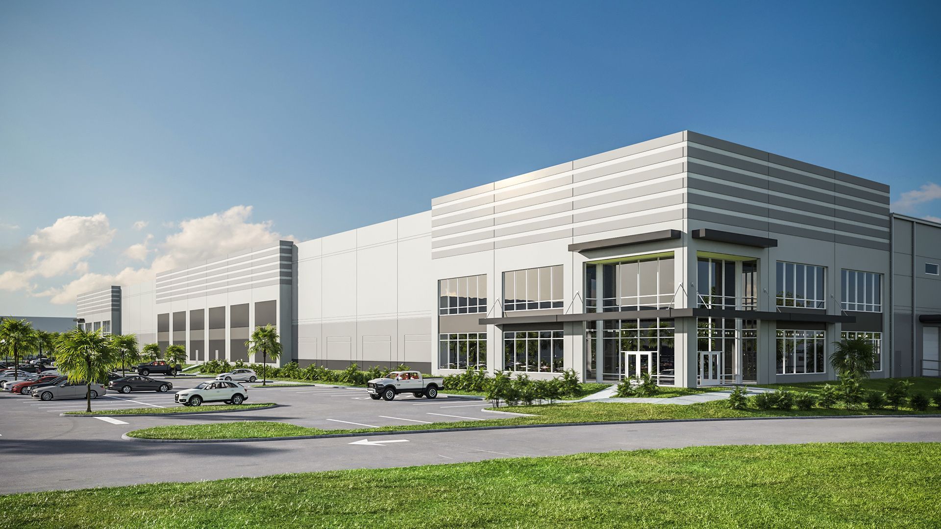 Large gray industrial building with office entrance, parking lot, and green grass.