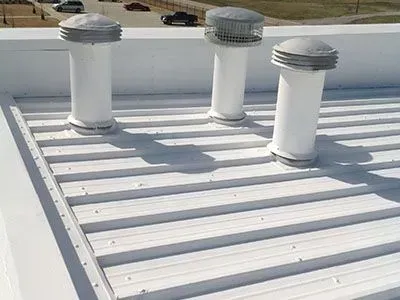Three white ventilation pipes on a white corrugated metal roof.