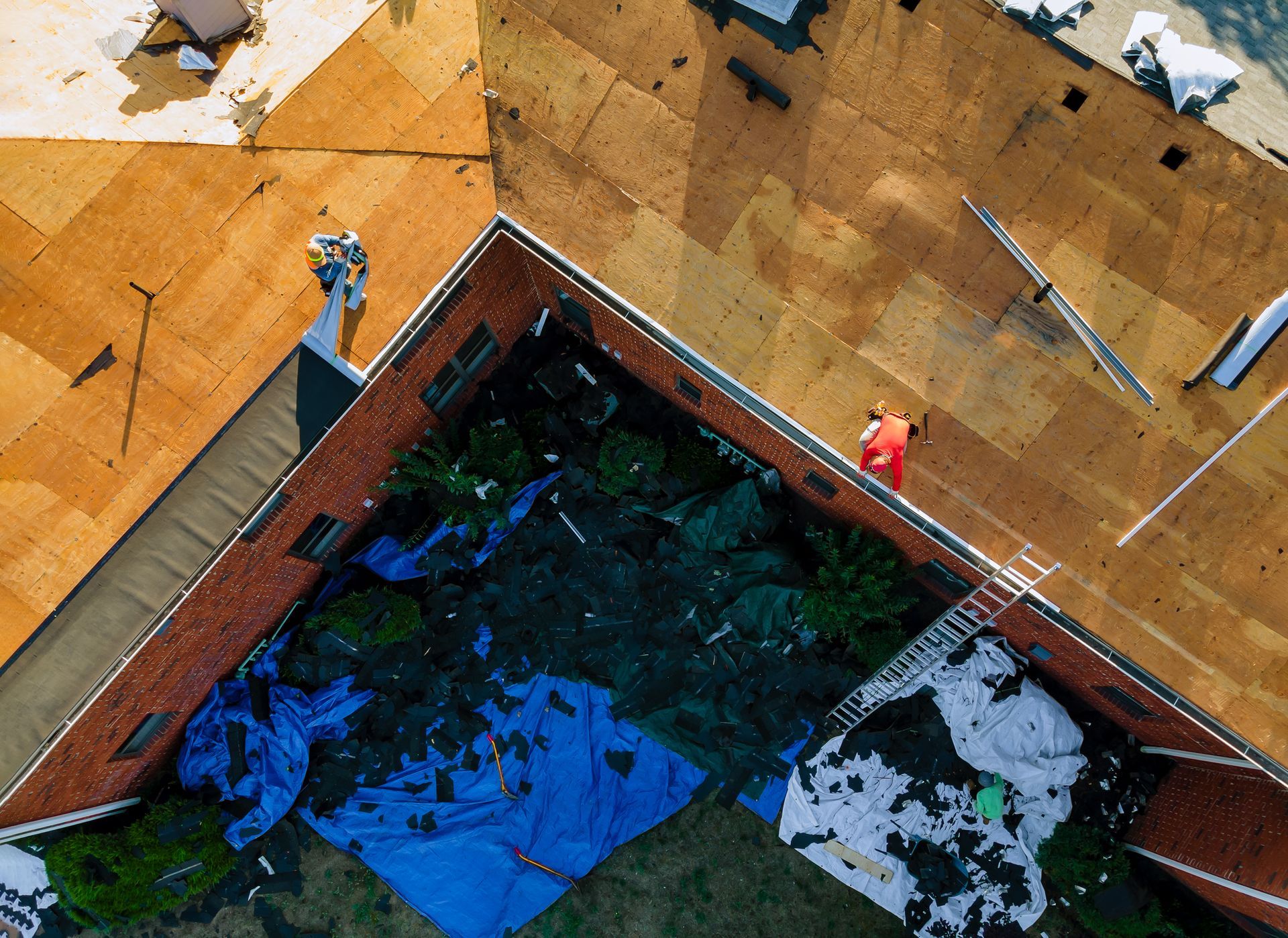 Overhead view of a building with exposed roof supports. A blue tarp covers a courtyard.