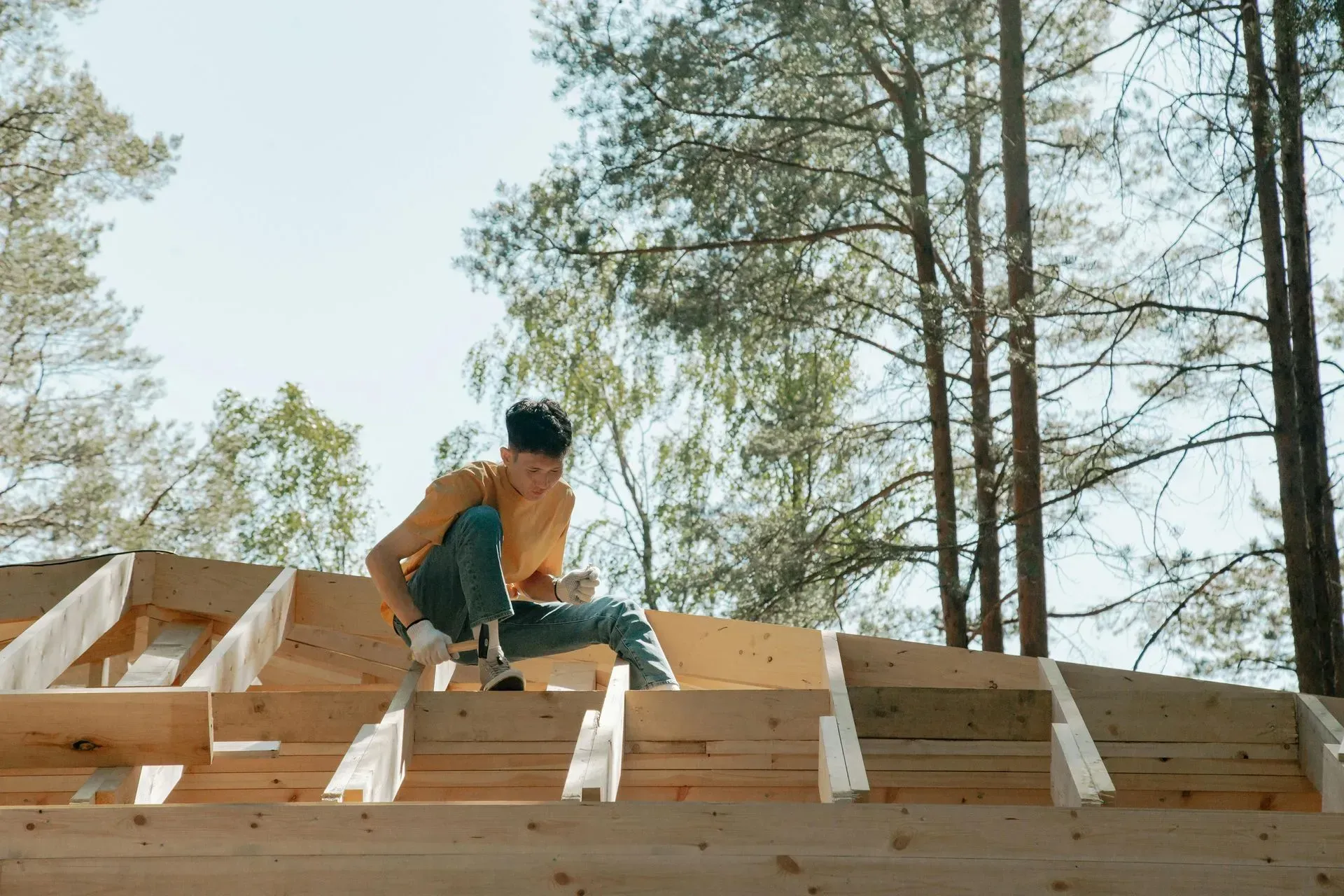 Person working on a wooden roof frame outdoors, sunlight.