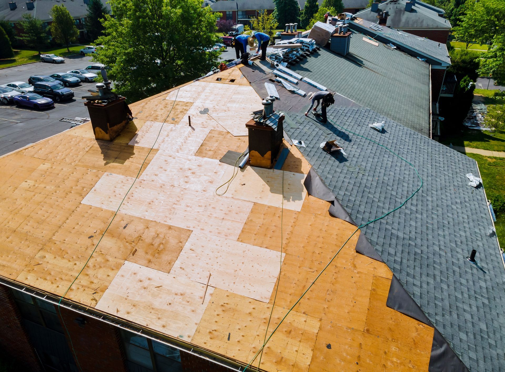 Roofers working on a building roof, partially covered in new shingles. Brown and gray shingles are visible.