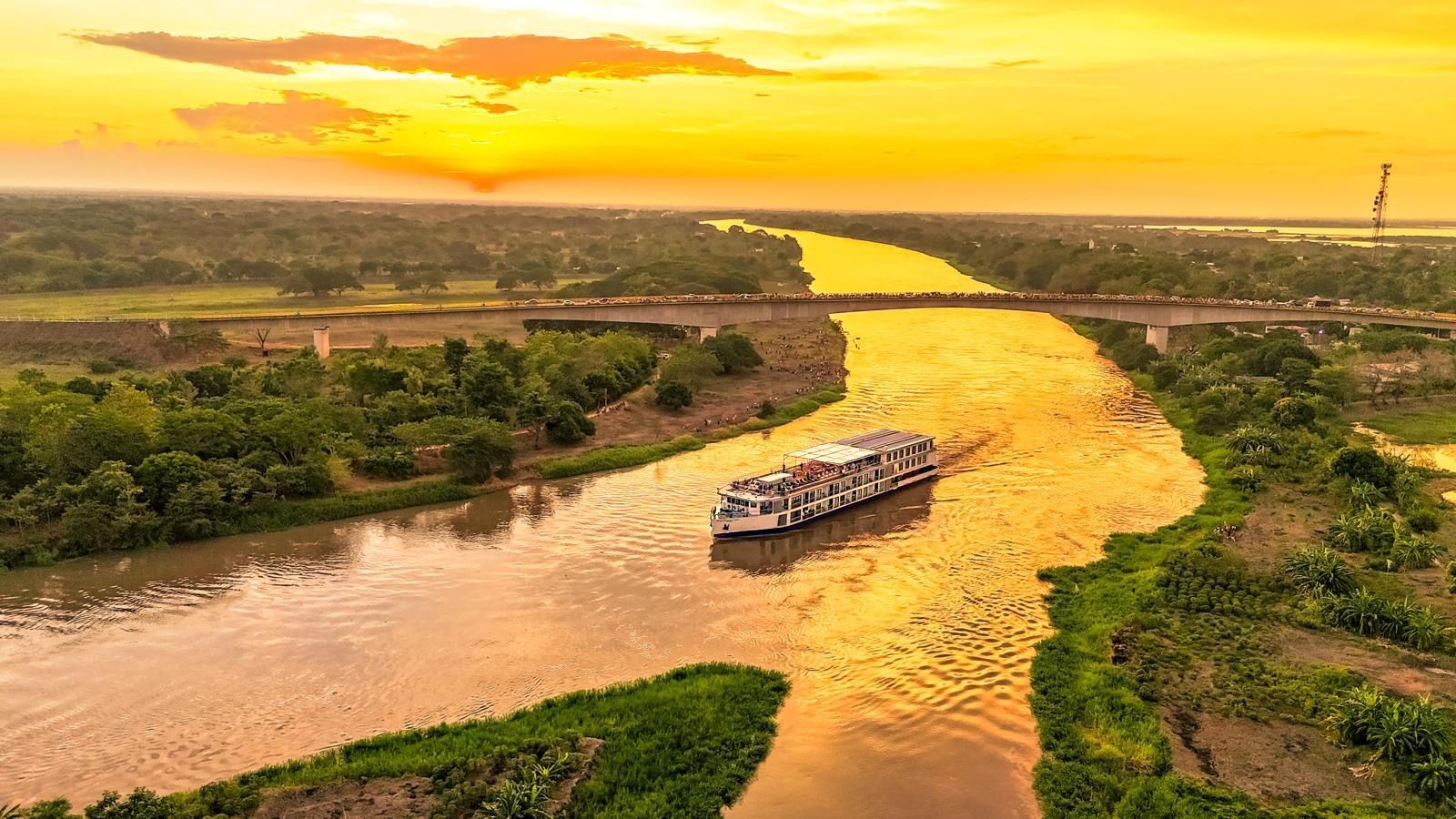 An aerial view of a boat traveling down a river at sunset.