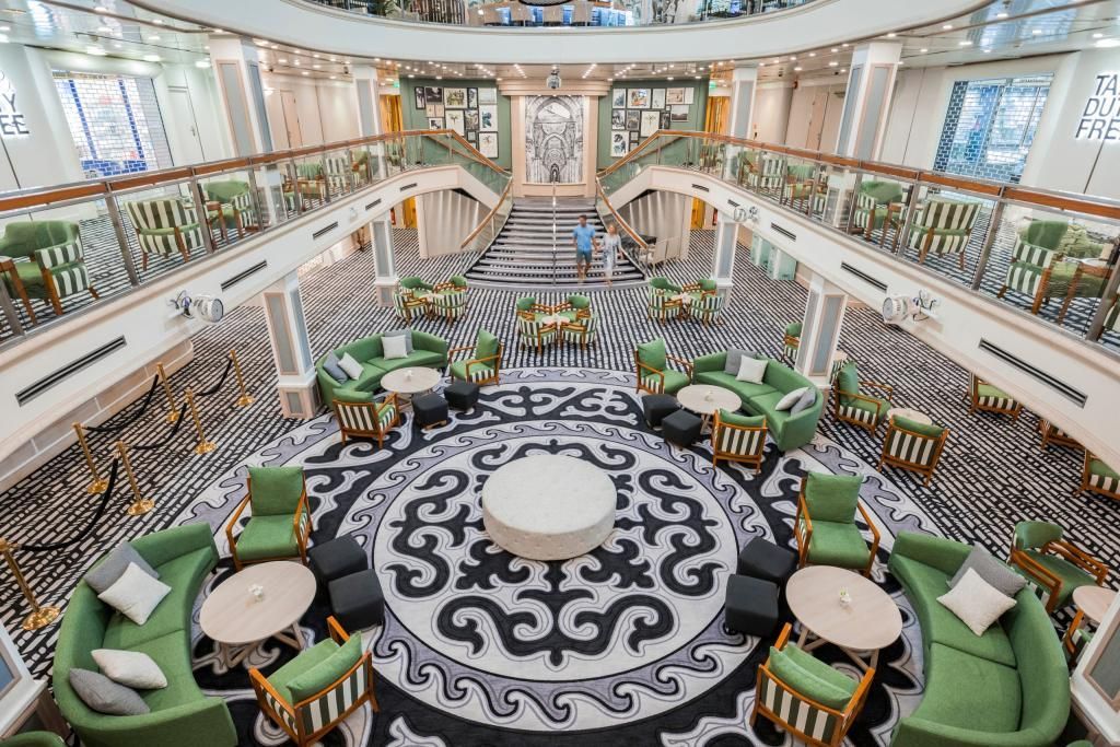 A large lobby on a cruise ship with green chairs and tables.