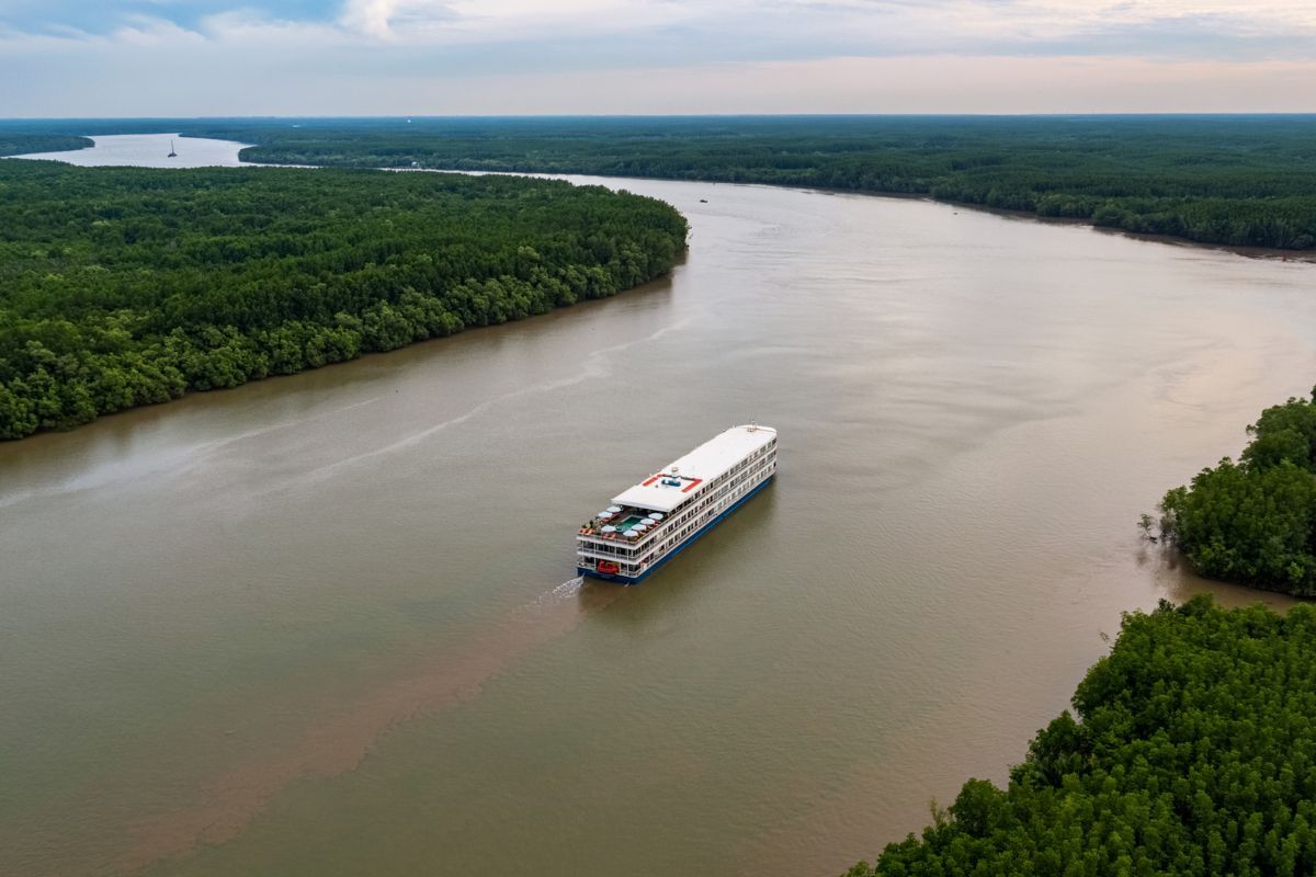 An aerial view of a cruise ship sailing down a river surrounded by trees.