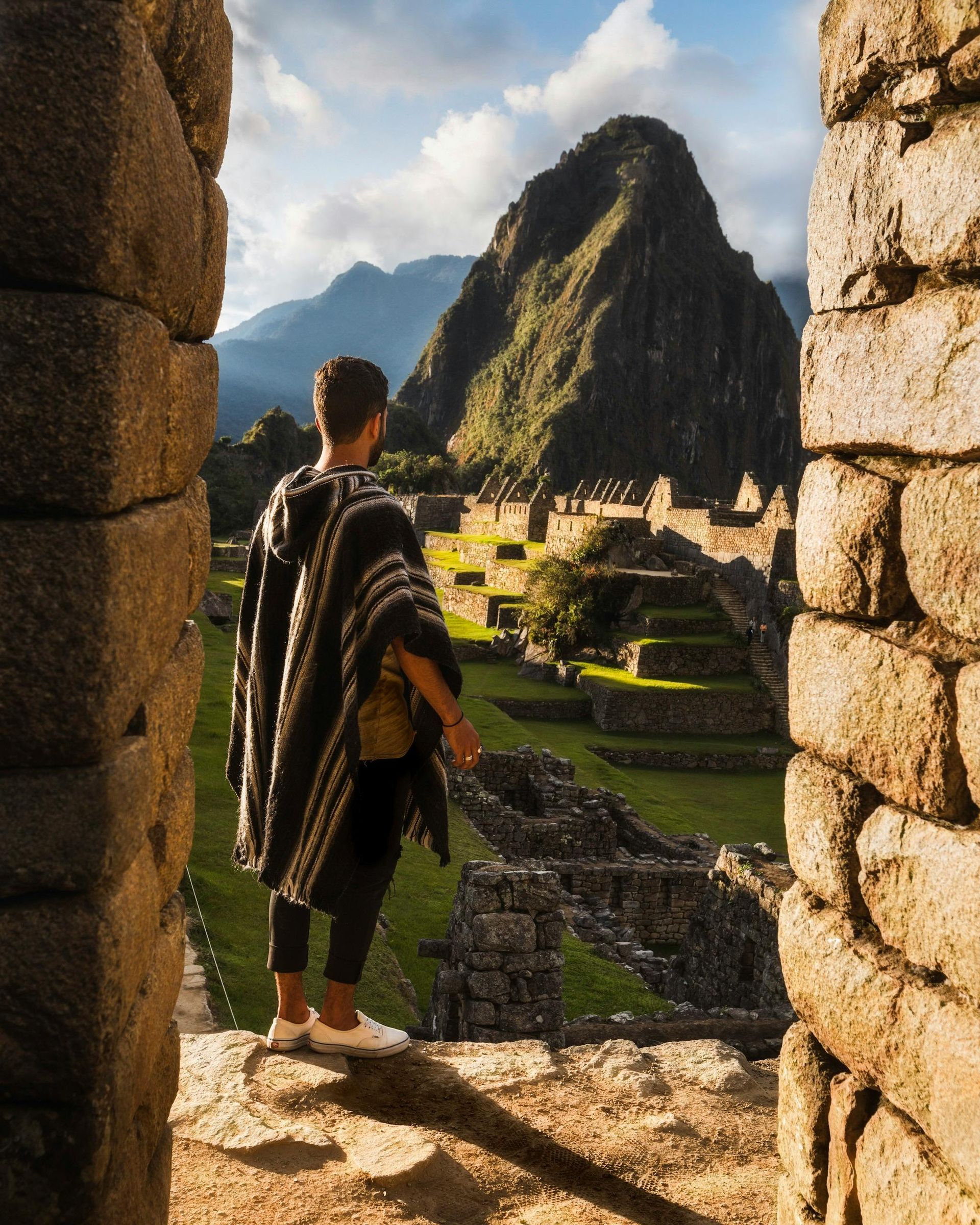 A man in a poncho is standing in front of a mountain.