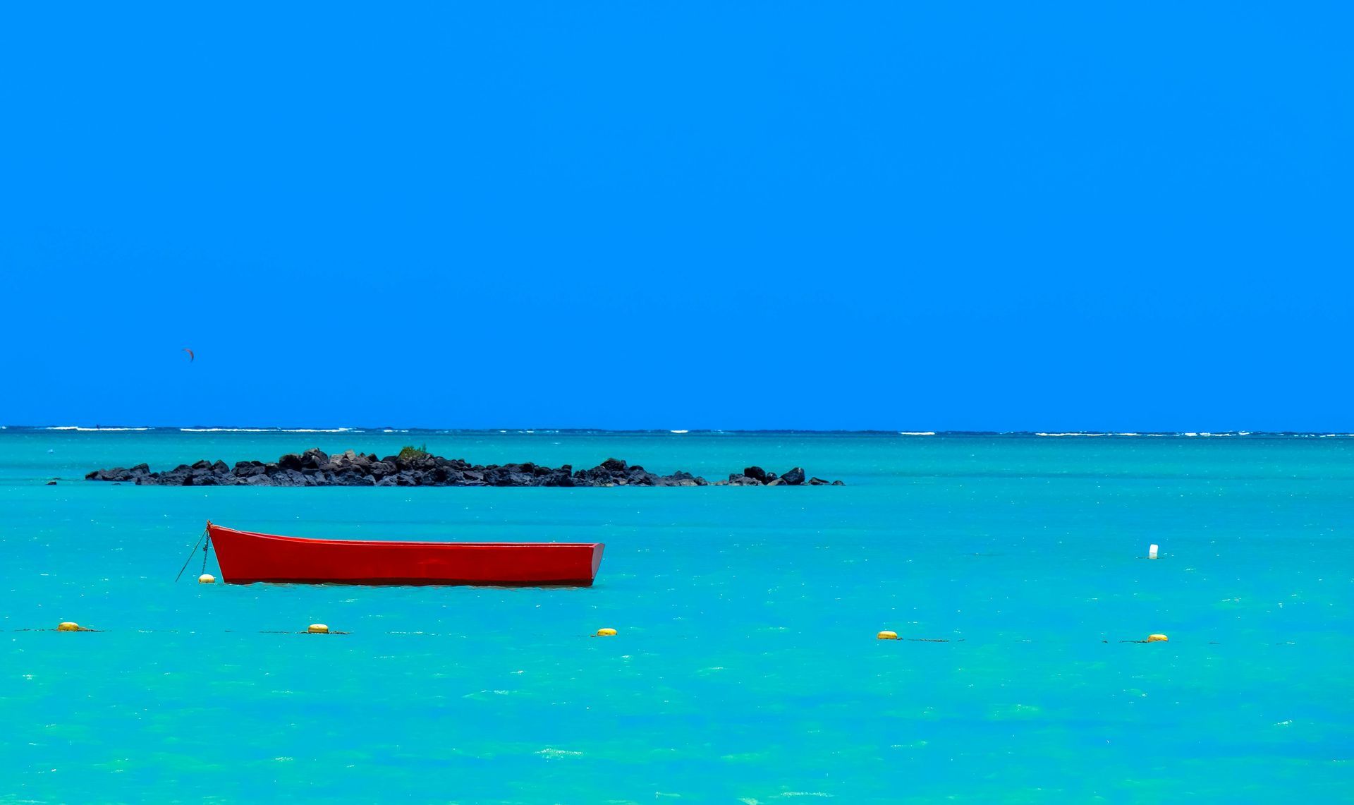 A red boat is floating on top of a turquoise ocean.