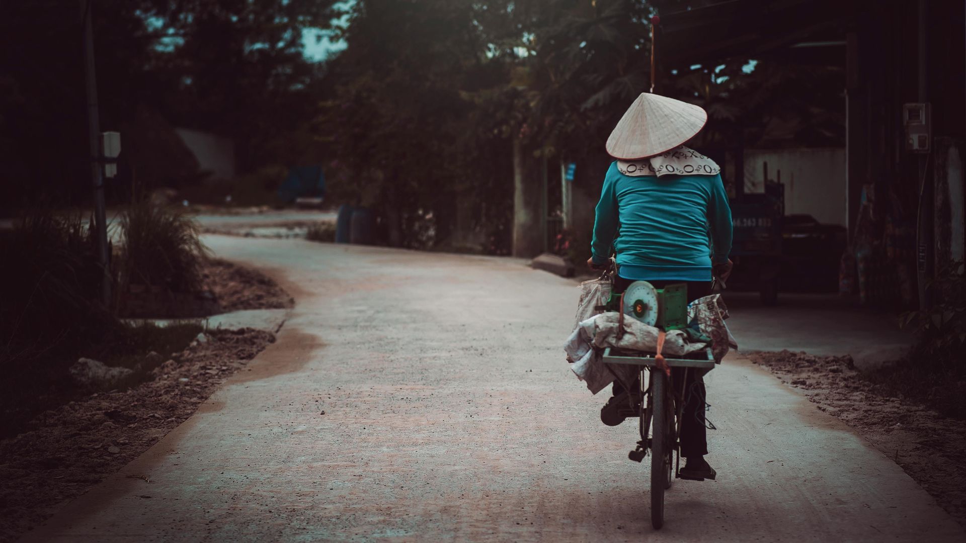 A woman wearing a conical hat is riding a bicycle down a road.