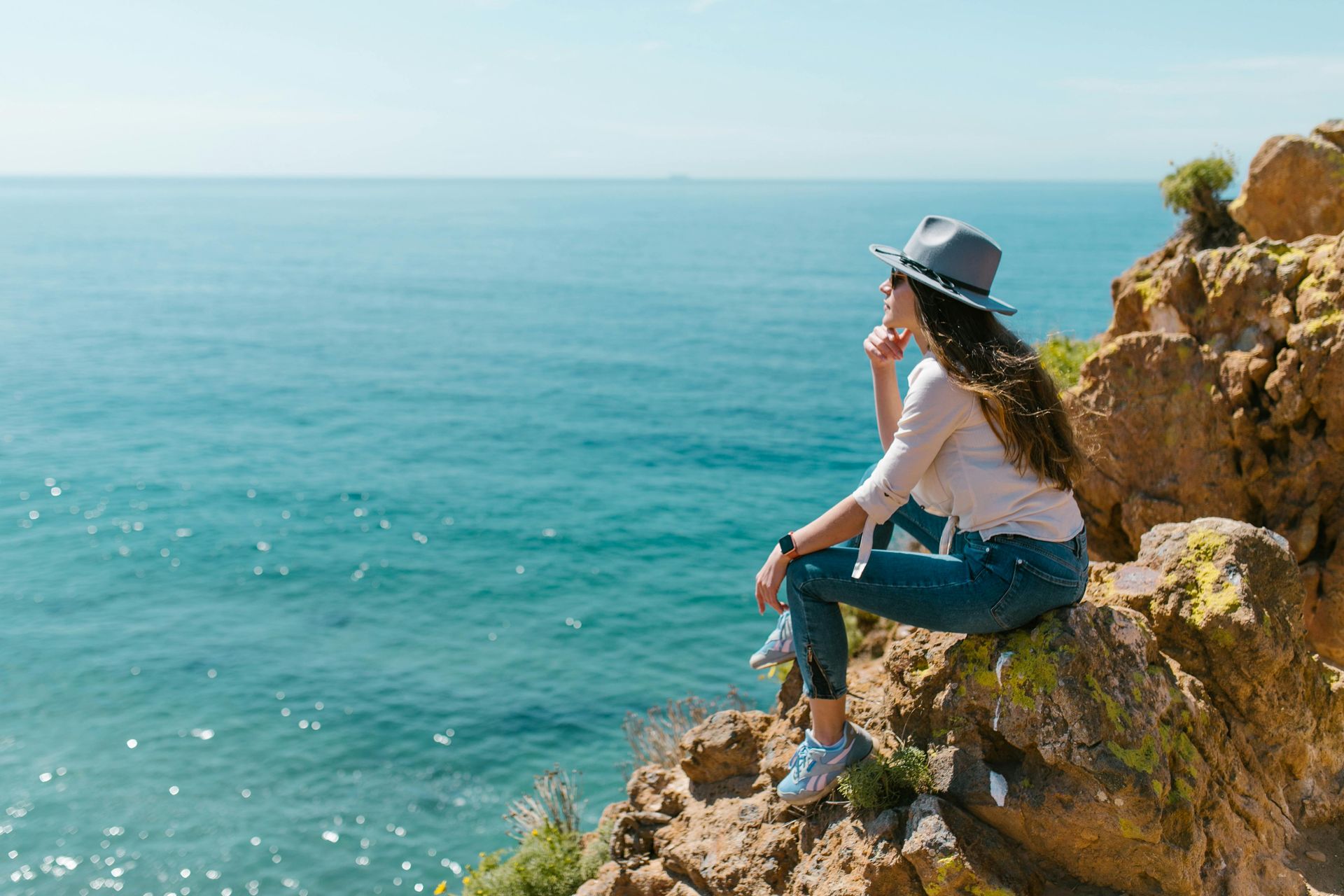 A woman is sitting on a rock overlooking the ocean.
