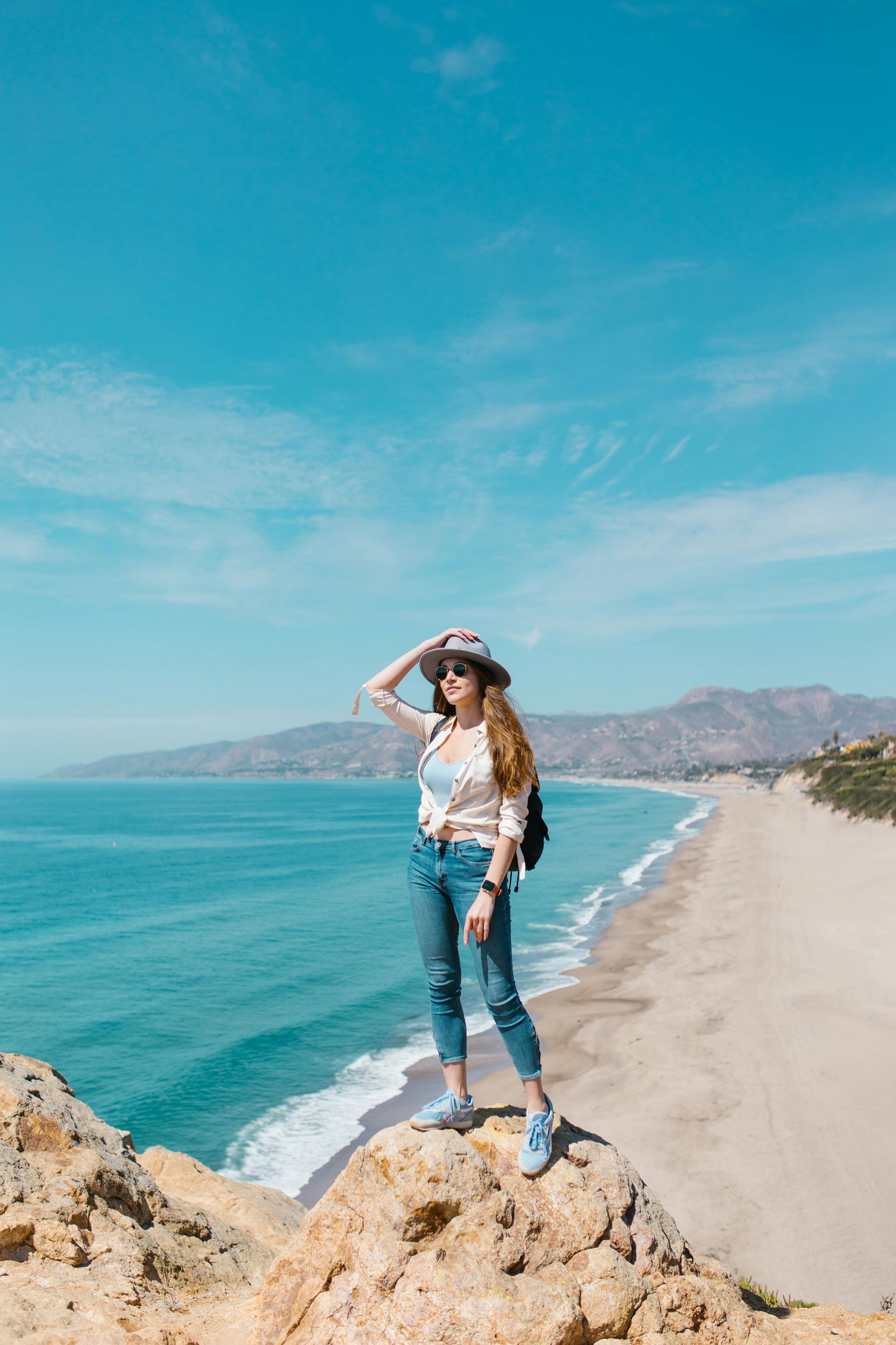 A woman is standing on top of a cliff overlooking the ocean.