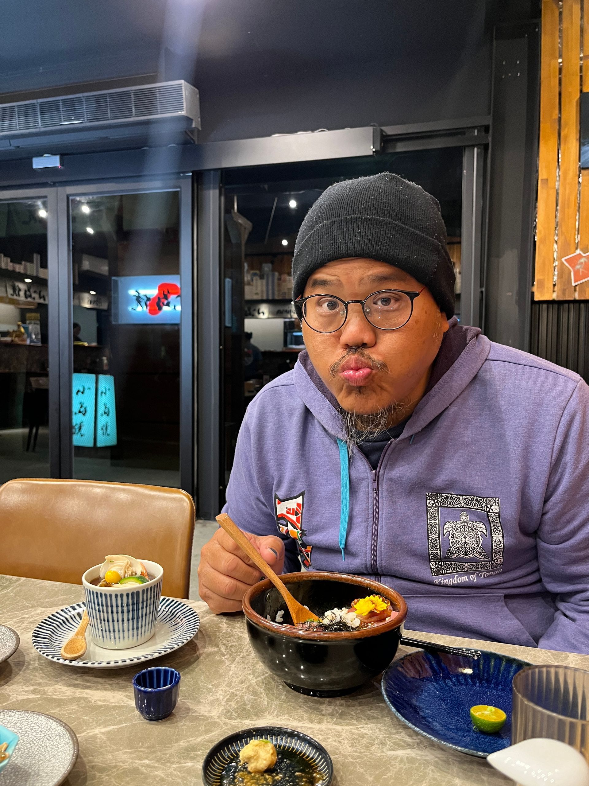 a man wearing glasses and a beanie is sitting at a table eating food .