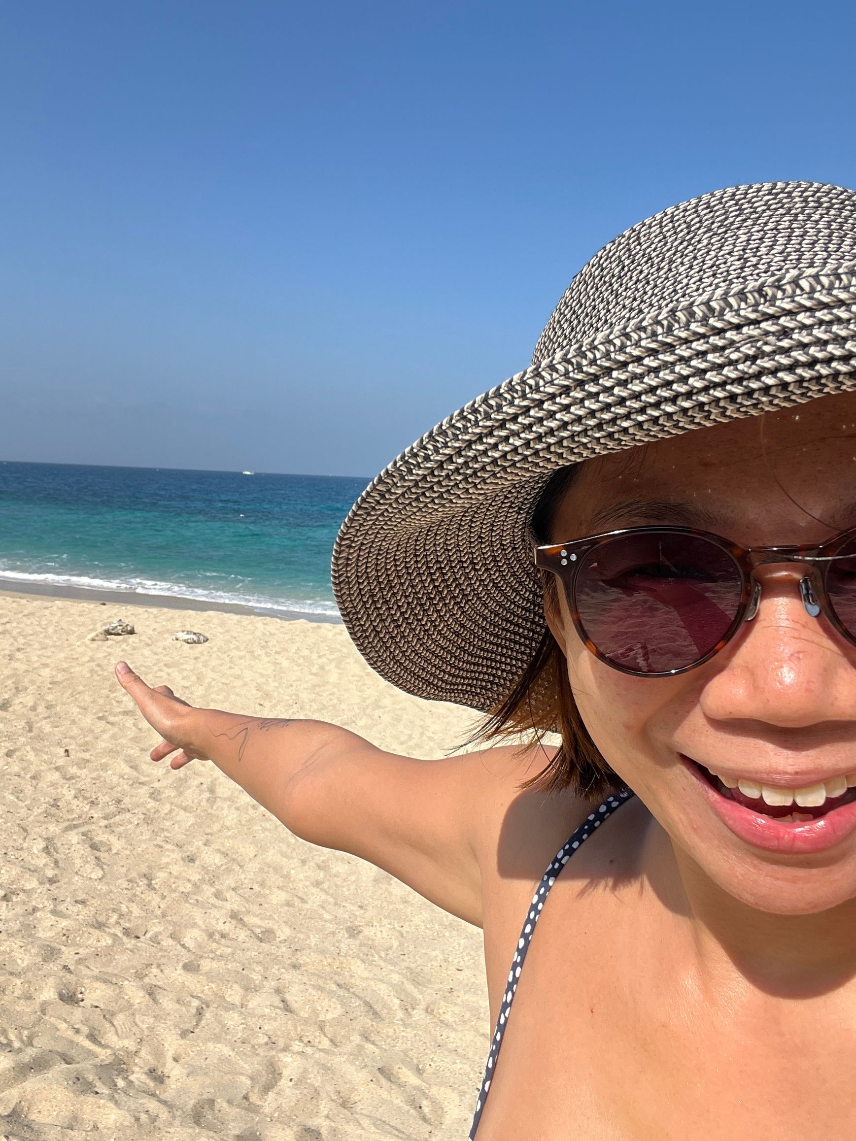 a woman wearing a hat and sunglasses is standing on Zhongao Beach on Xiaoliuqiu