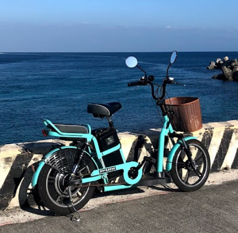 A blue bicycle with a basket is parked on the side of the road next to the ocean.