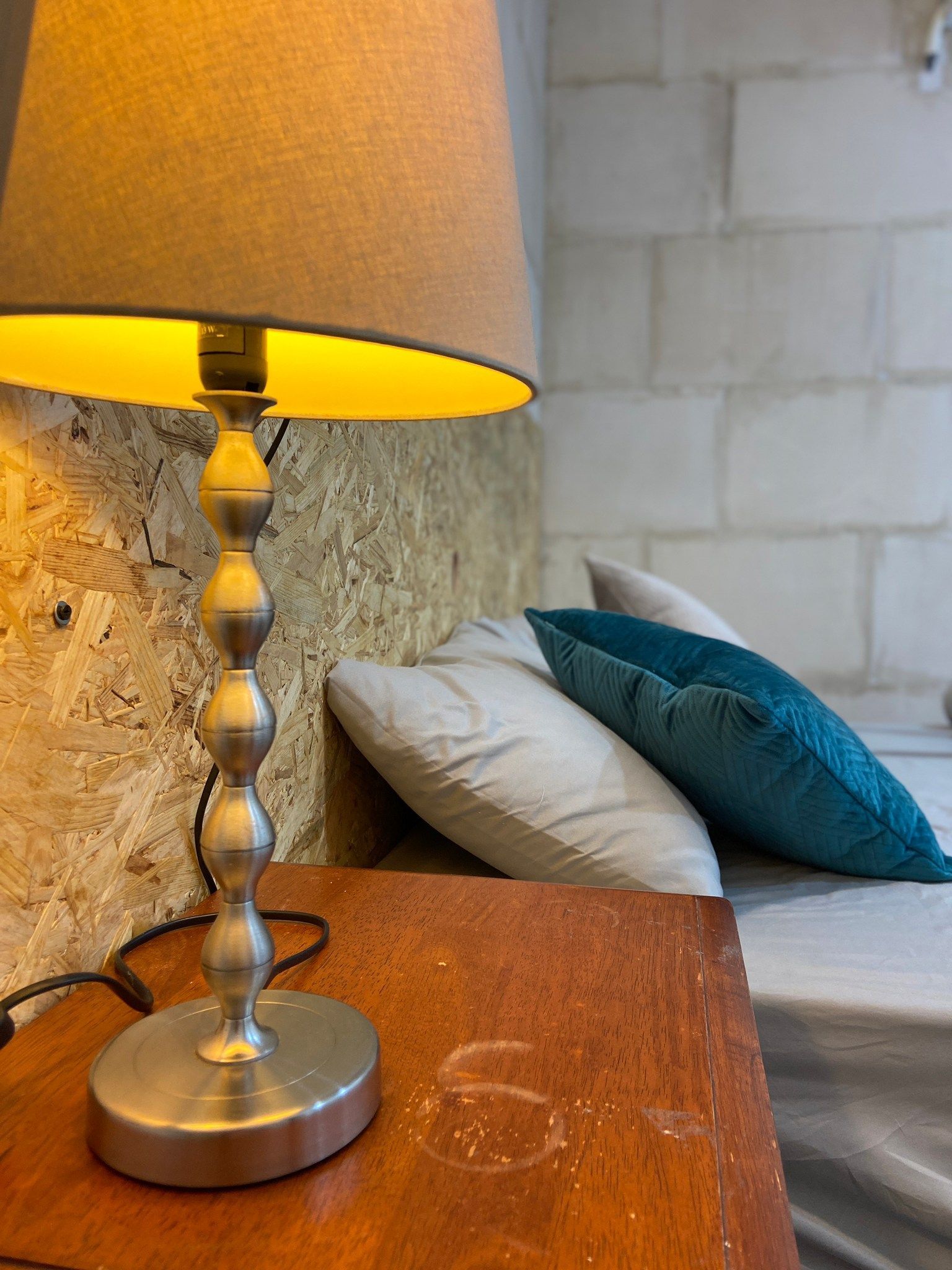 A lamp is sitting on a wooden table next to a bed.