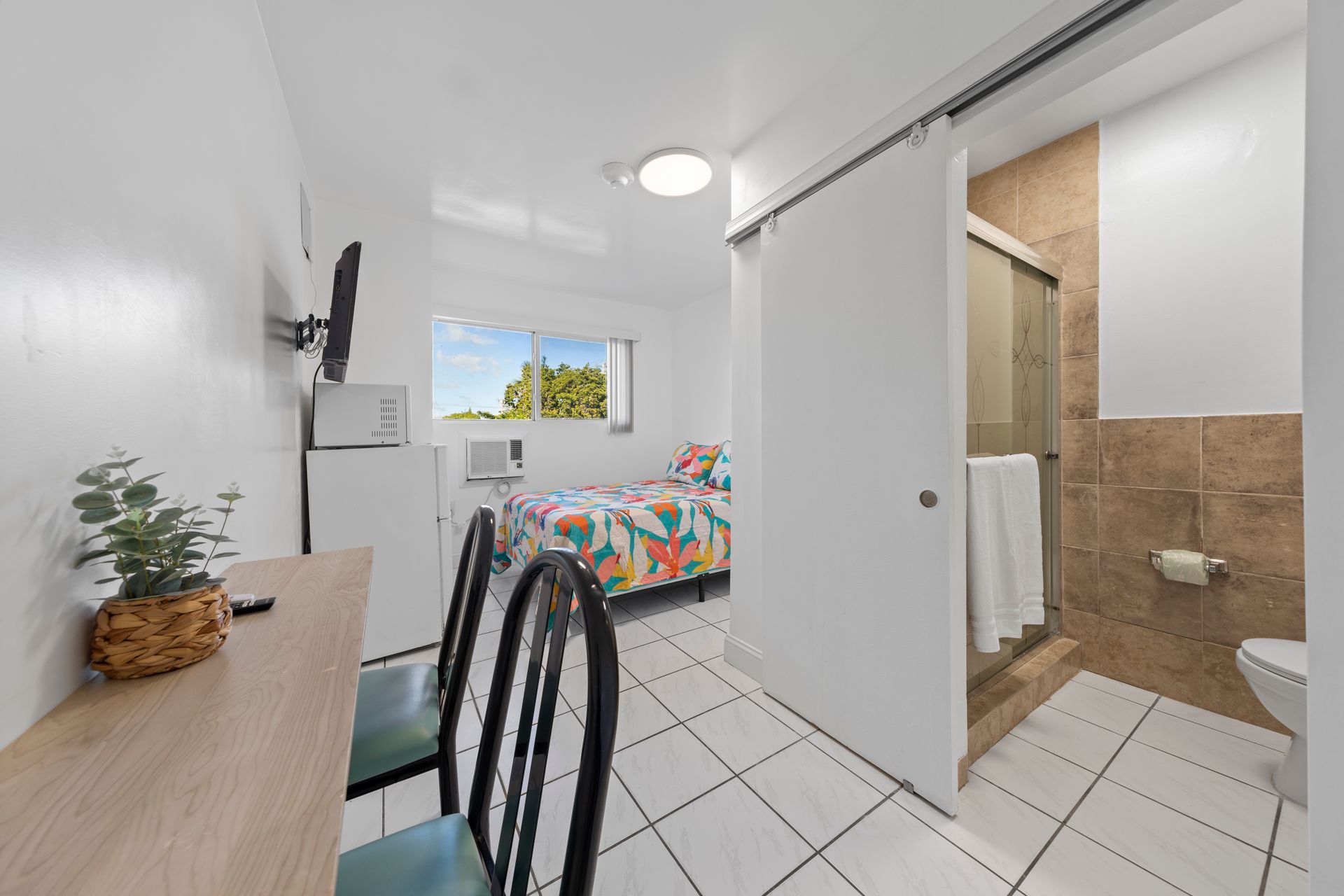 Small hotel room with bed, table, chairs, microwave, TV, and bathroom.