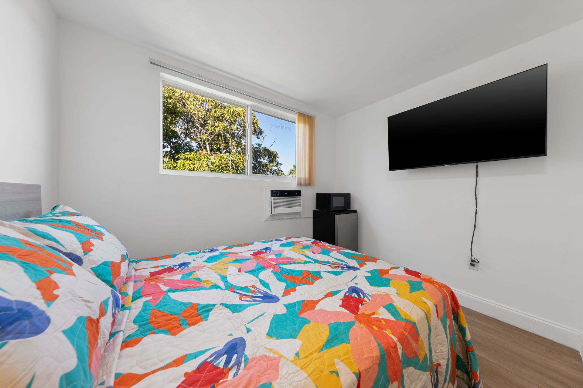 Bedroom with floral bedspread, TV, window, and mini-fridge.