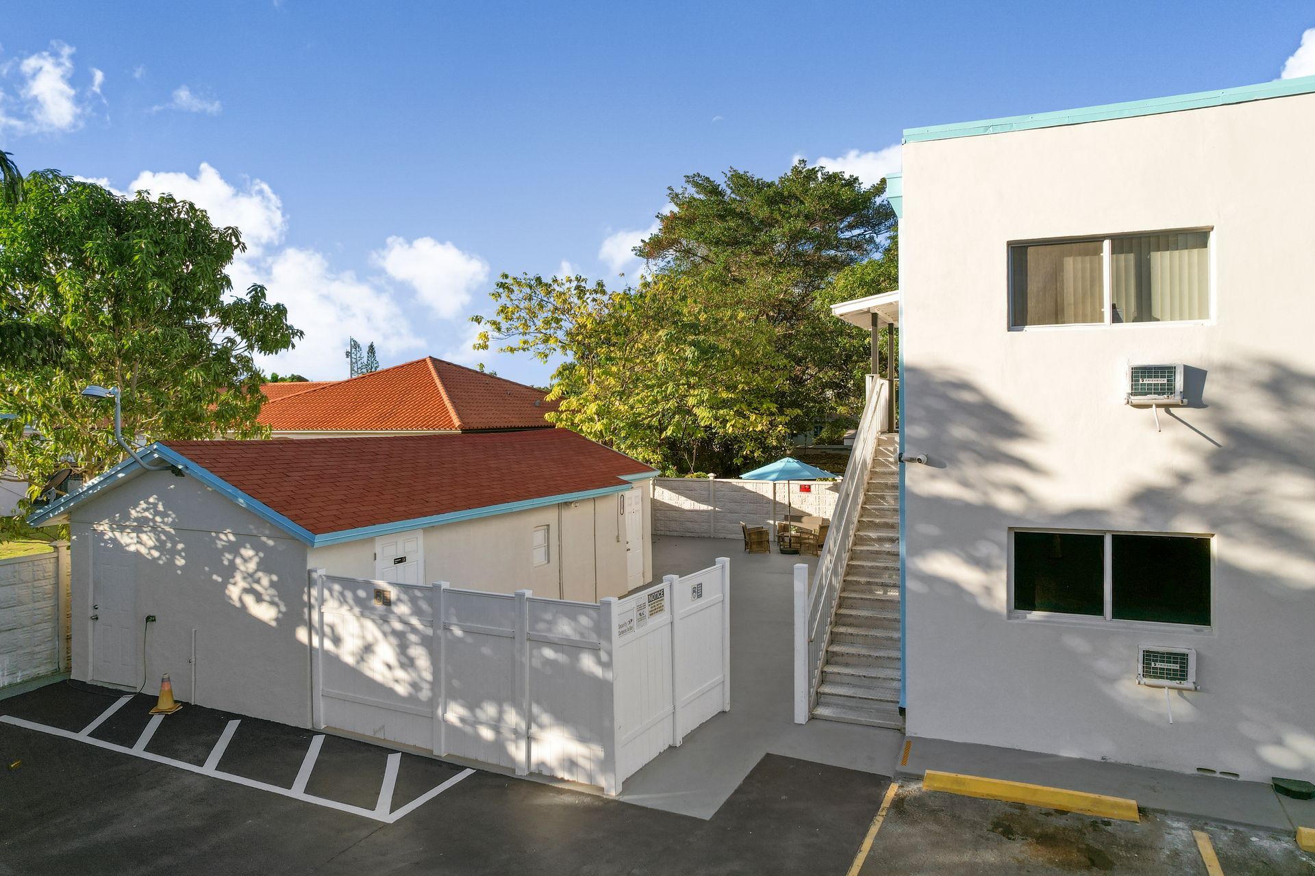 Exterior view of white building with stairs, fenced area, and parking spots. Blue sky.
