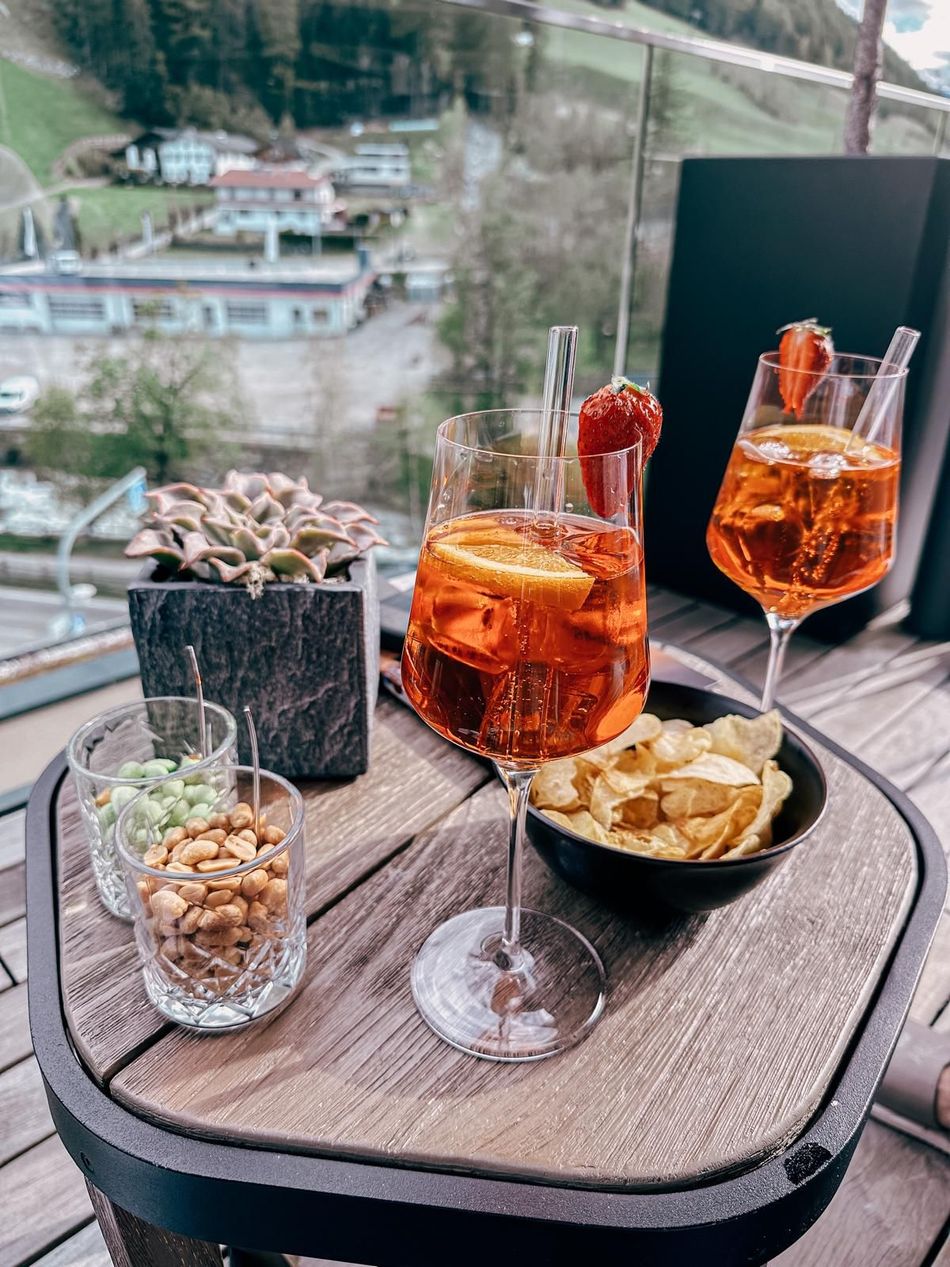 Zwei Aperol Spritz mit Snacks auf einem Tisch vor malerischer Kulisse.
