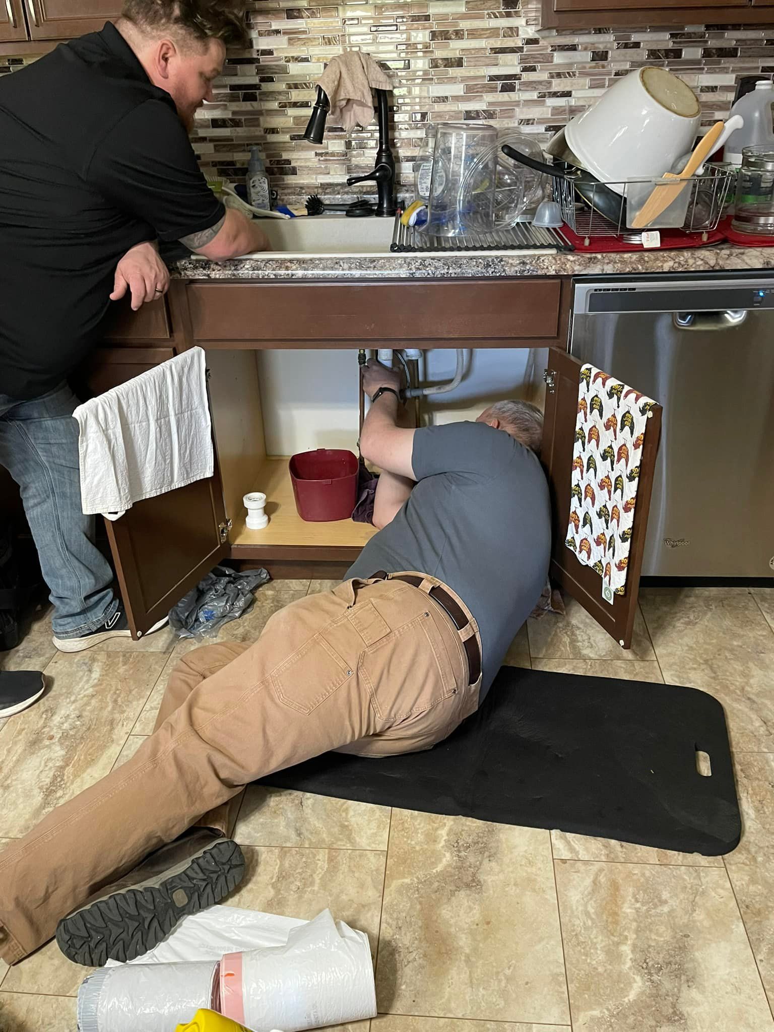 Two men are working under a sink in a kitchen.