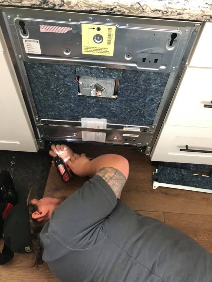A man is fixing a dishwasher in a kitchen.