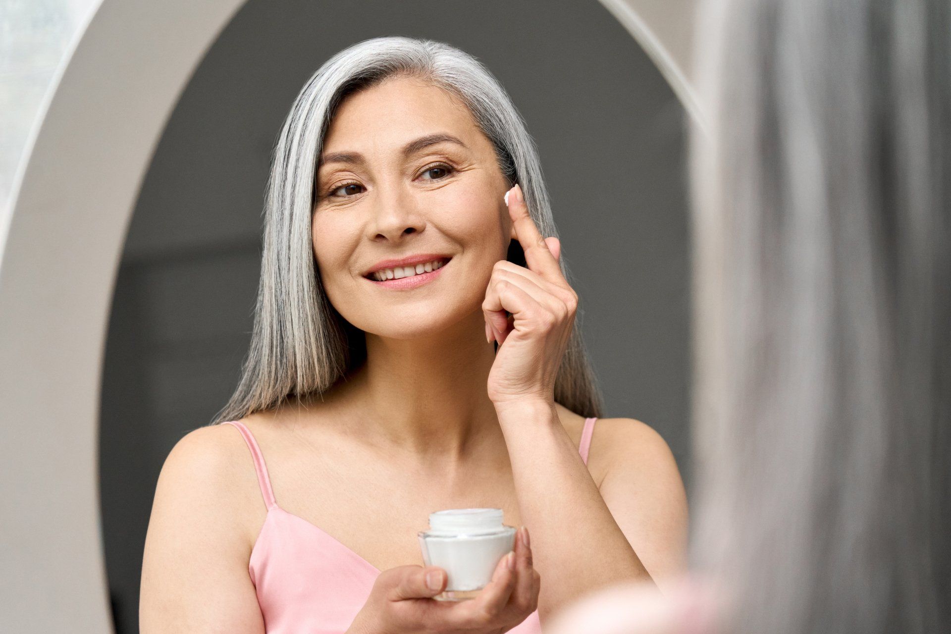happy middle aged mature asian woman applying face cream