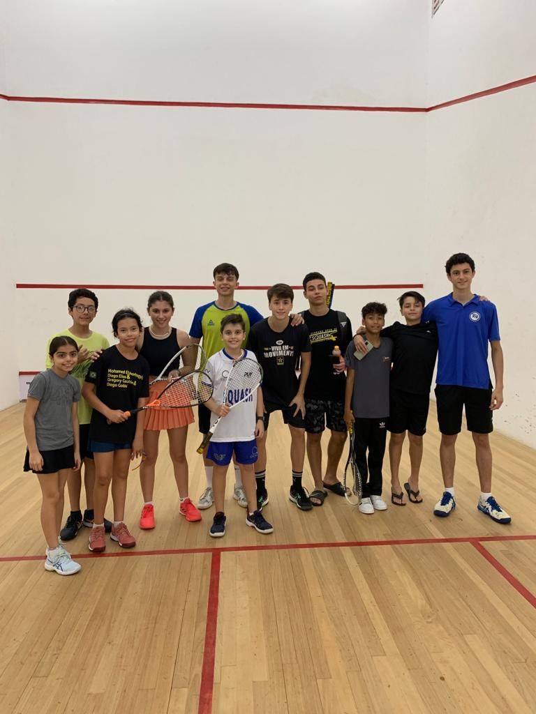 Um grupo de jovens está posando para uma foto em uma quadra de squash.