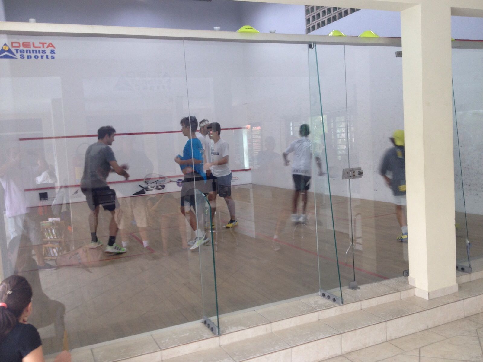 Um grupo de pessoas está jogando squash em uma sala com um logotipo da Delta na parede
