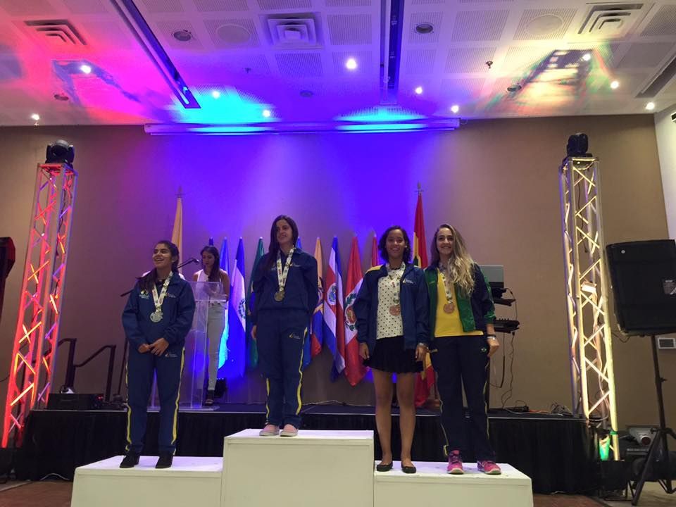 Um grupo de mulheres está em um pódio em frente a bandeiras.
