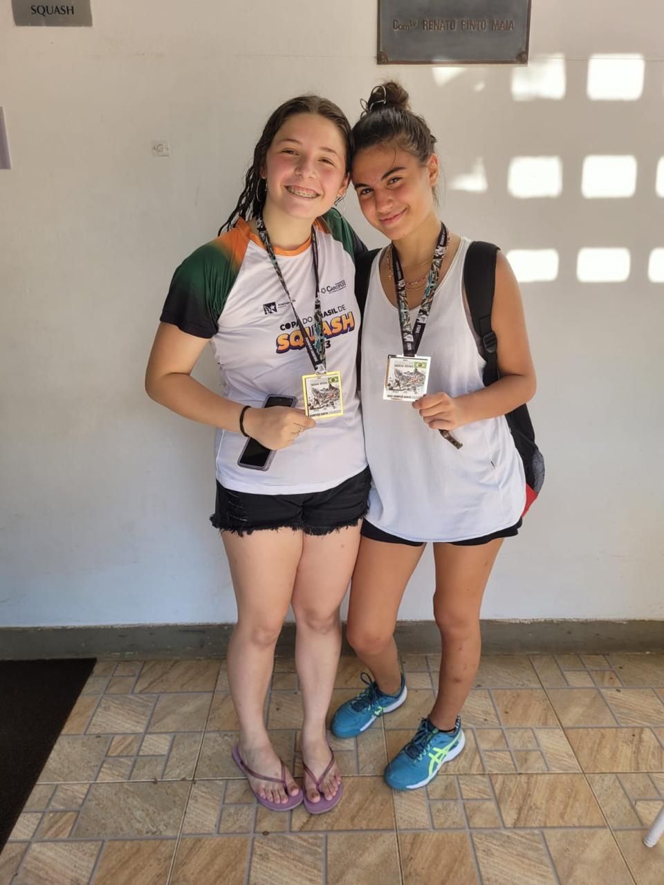 Duas meninas de pé uma ao lado da outra segurando medalhas
